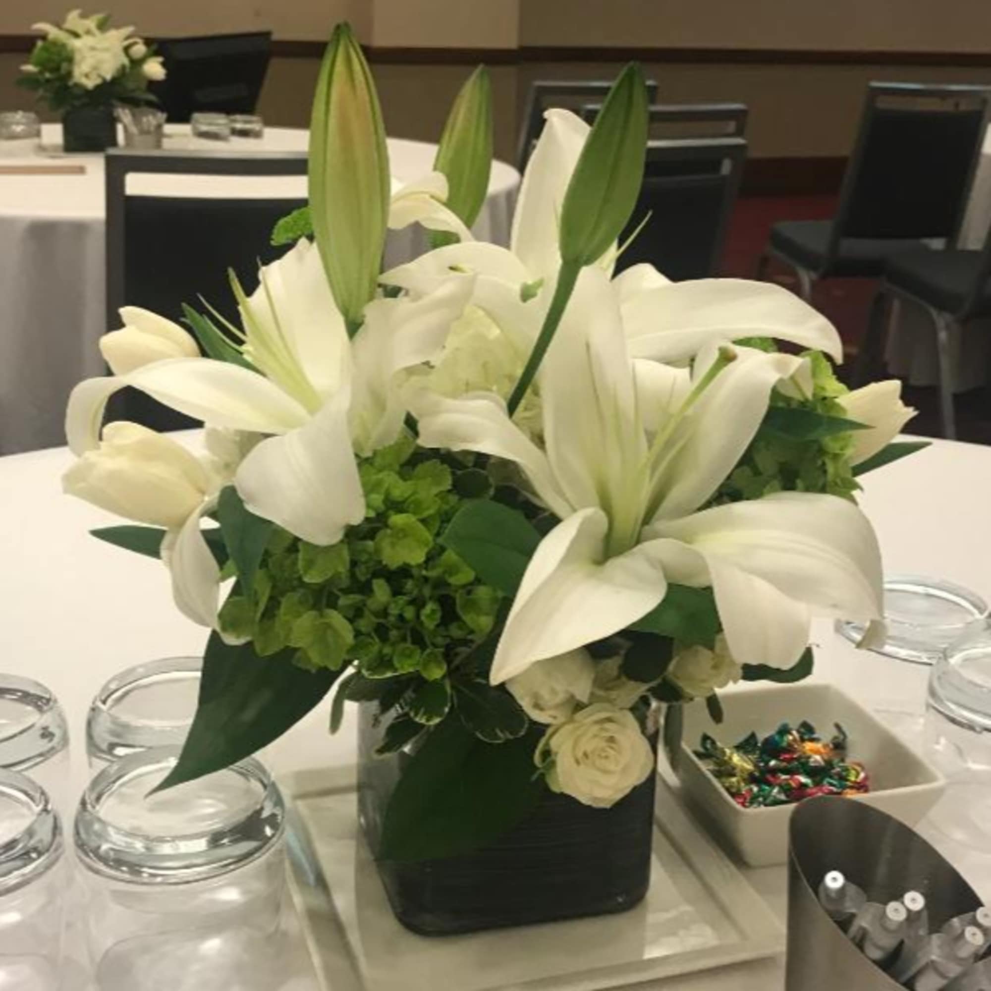 White lilies and roses in a black square vase on a table