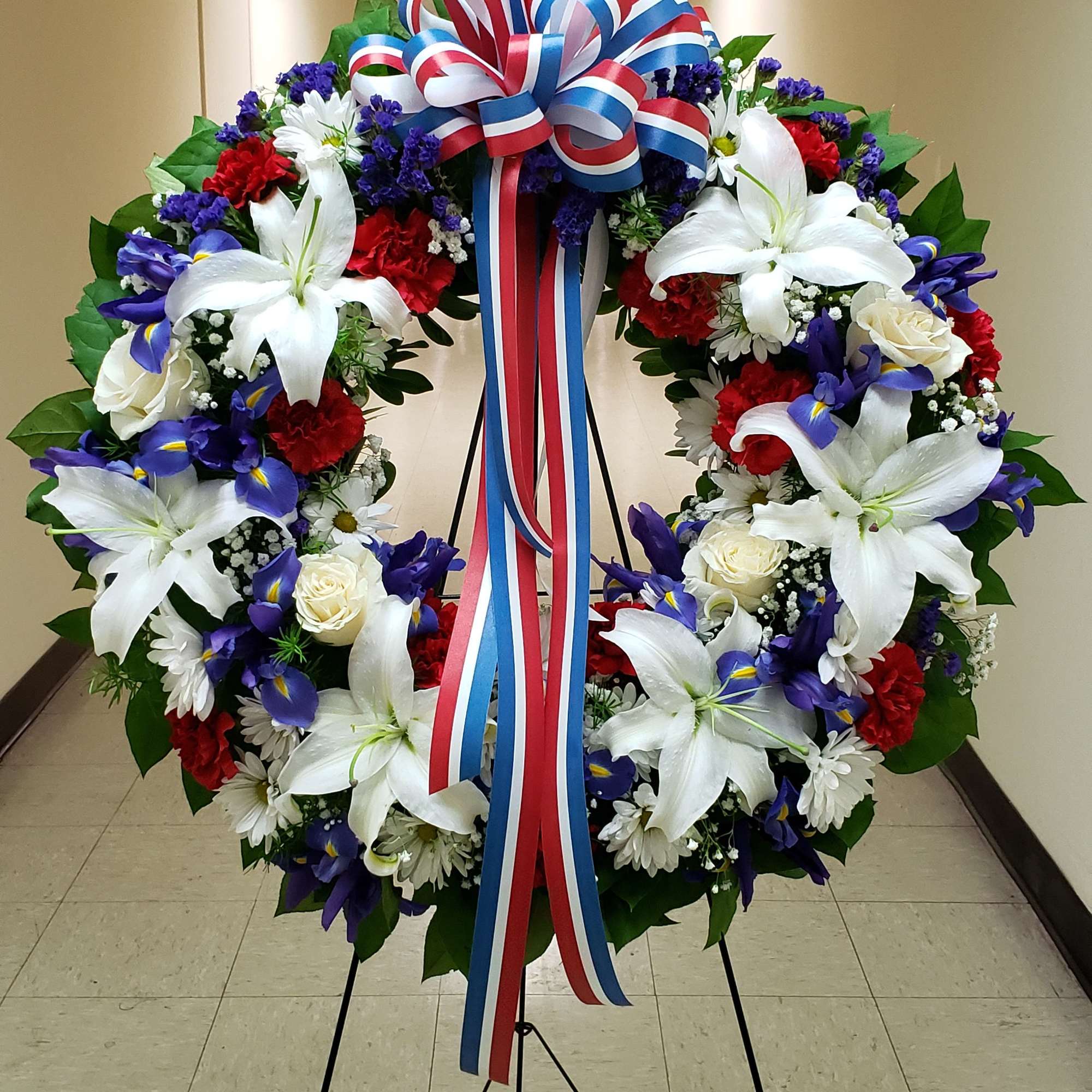 Large patriotic floral wreath on a stand with red, white, and blue ribbon