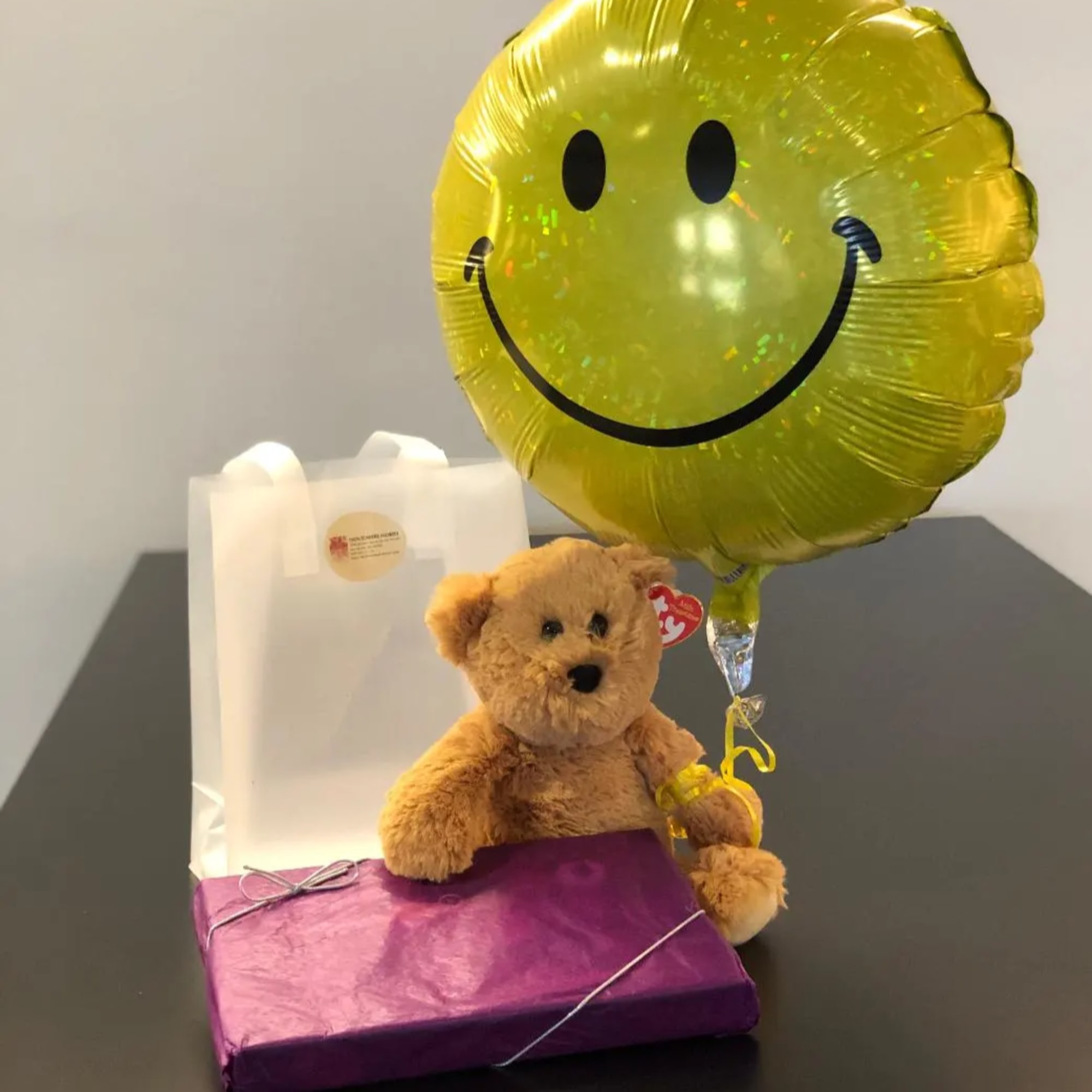 Teddy bear with a smiley-face balloon and gift boxes
