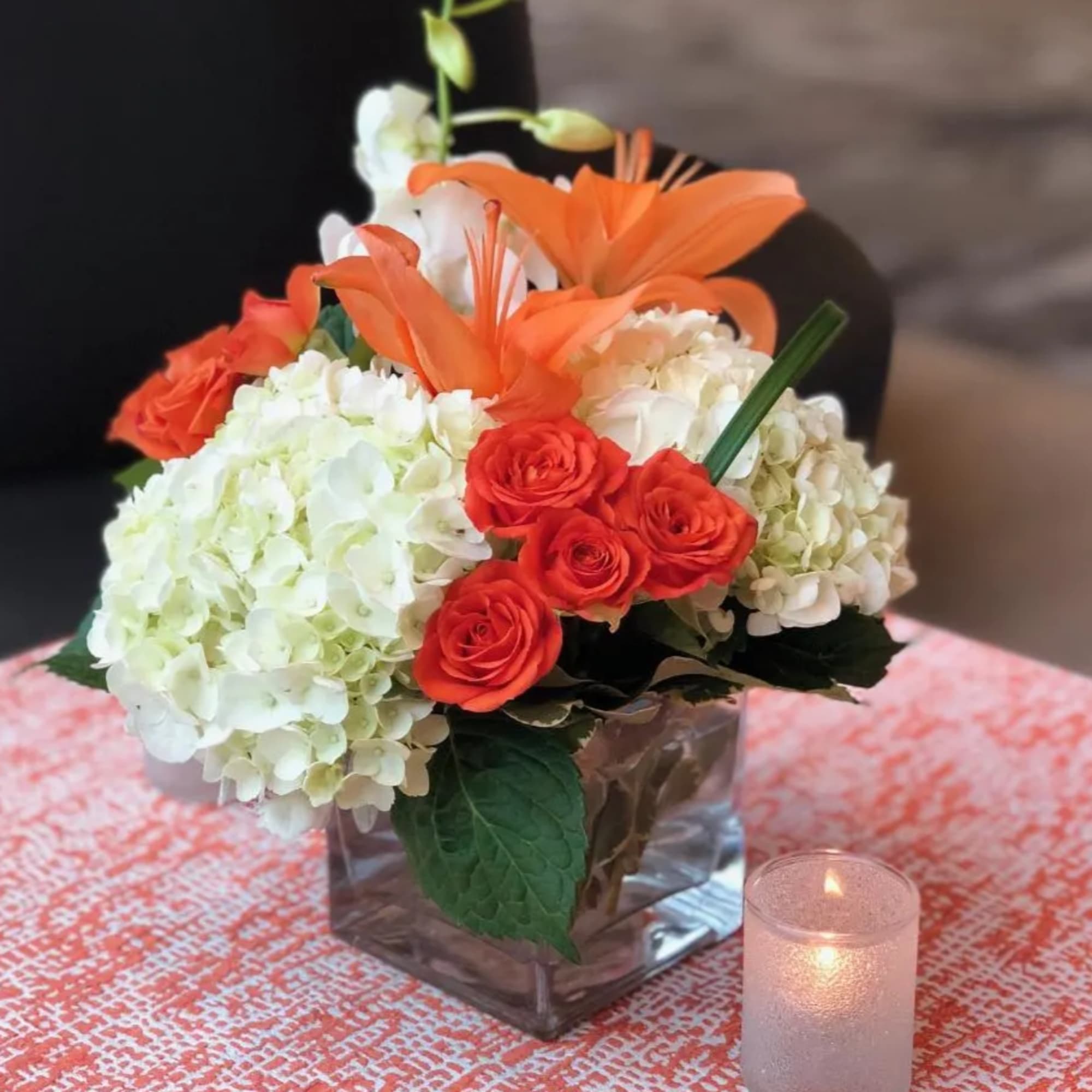 Orange lilies and red roses in a square glass vase with white hydrangeas