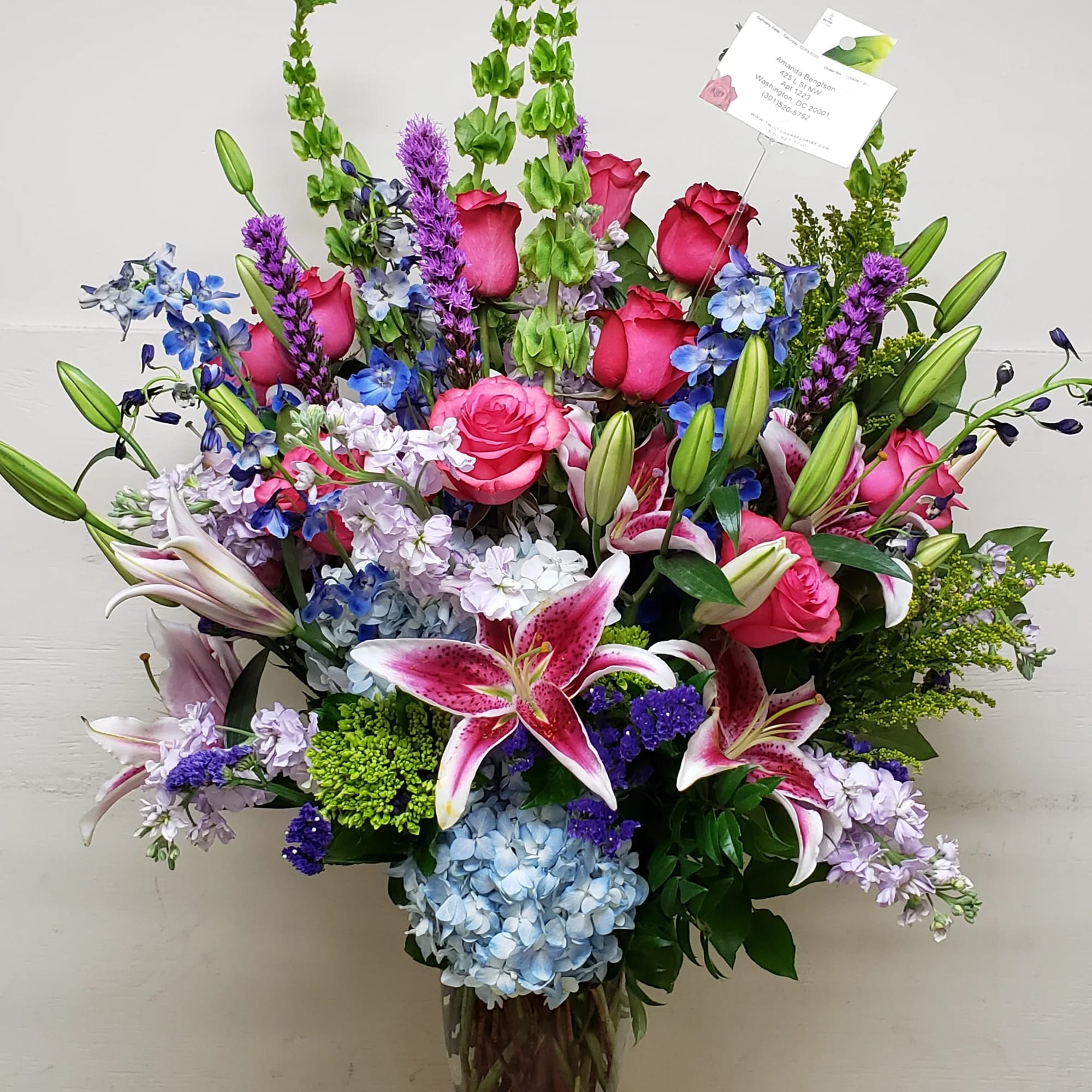 Large mixed bouquet in a glass vase with pink roses, lilies, and blue hydrangeas