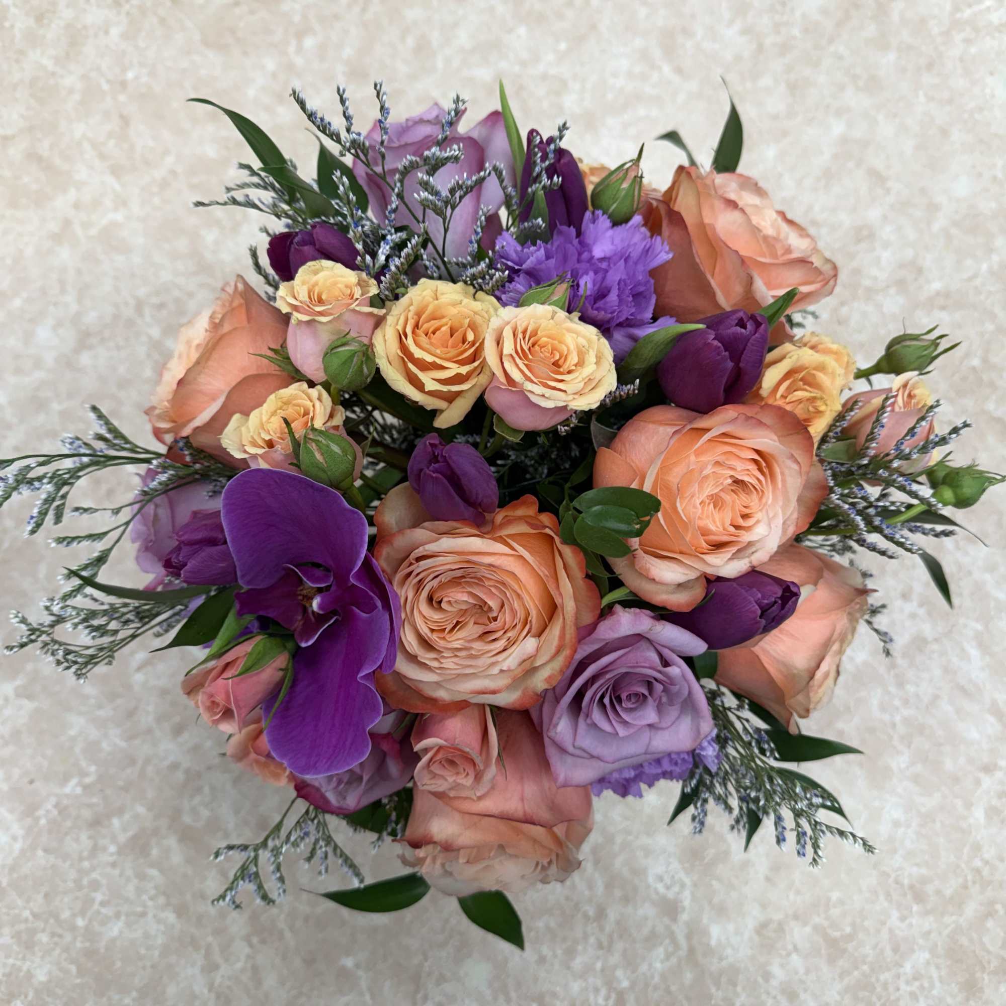 Bouquet of peach, lavender, and purple roses with purple orchids