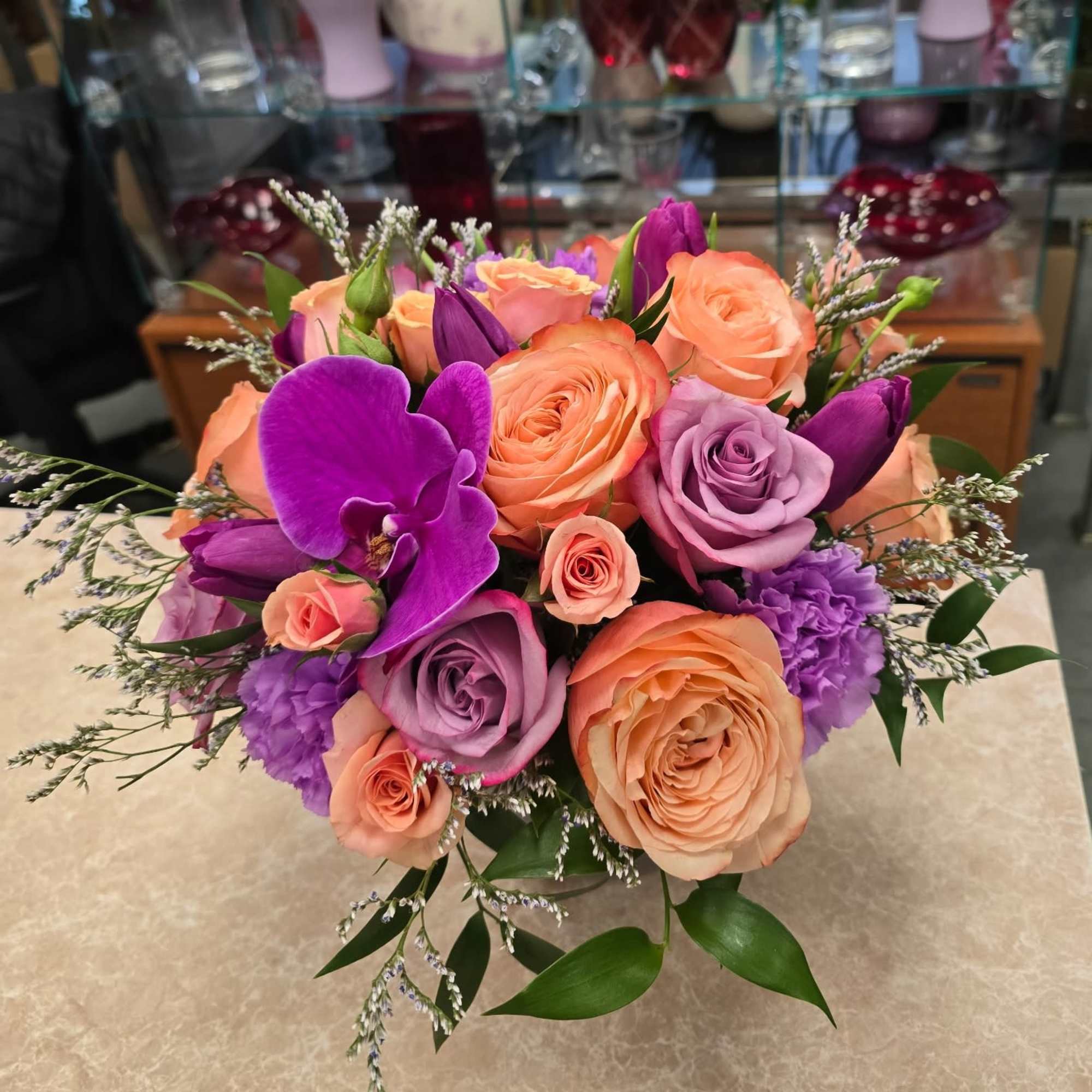 Bouquet of peach, lavender, and purple roses with orchids in a vase