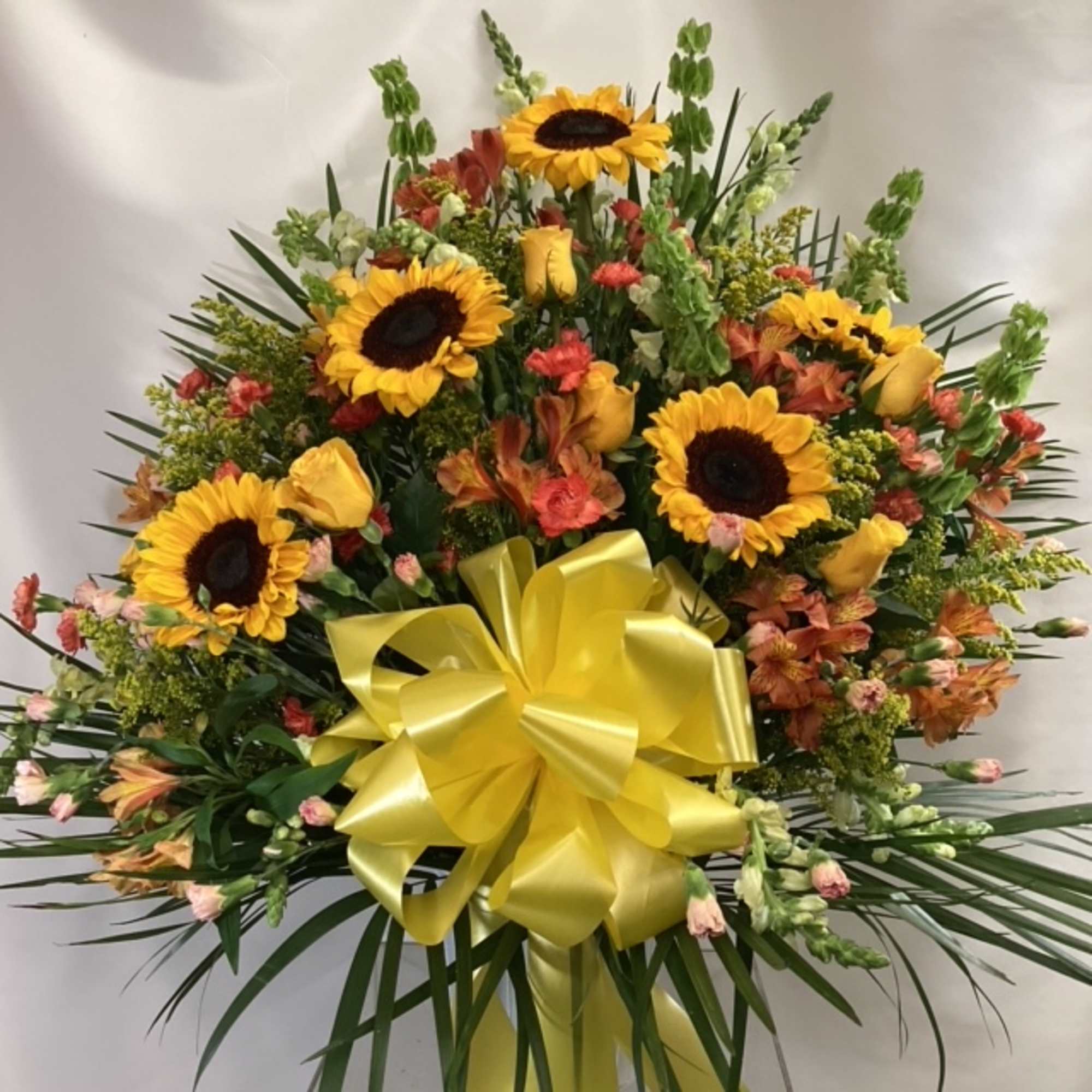 Large floral spray with sunflowers, yellow roses, and a yellow bow