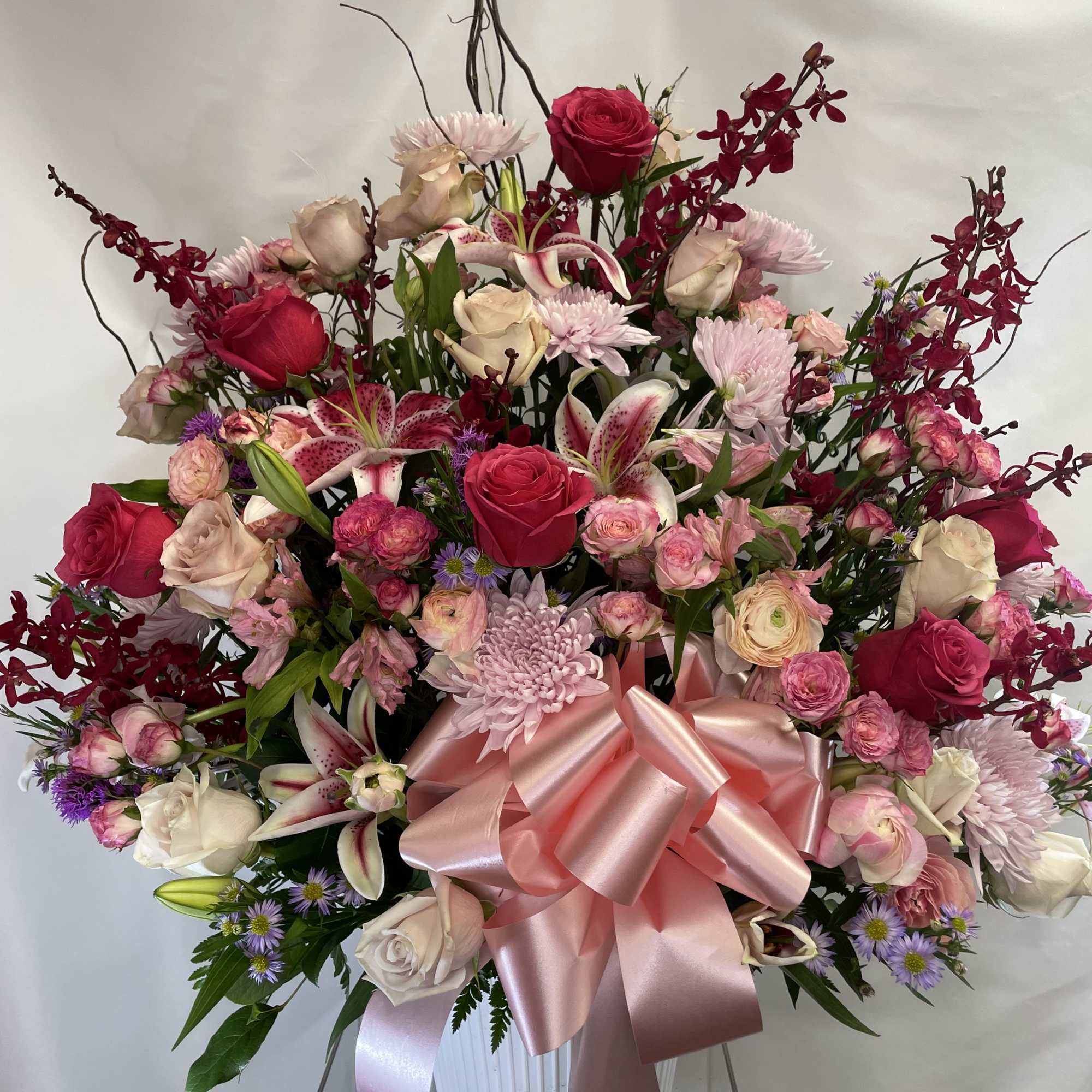 Large pink and white mixed flower arrangement with a satin bow in a white vase