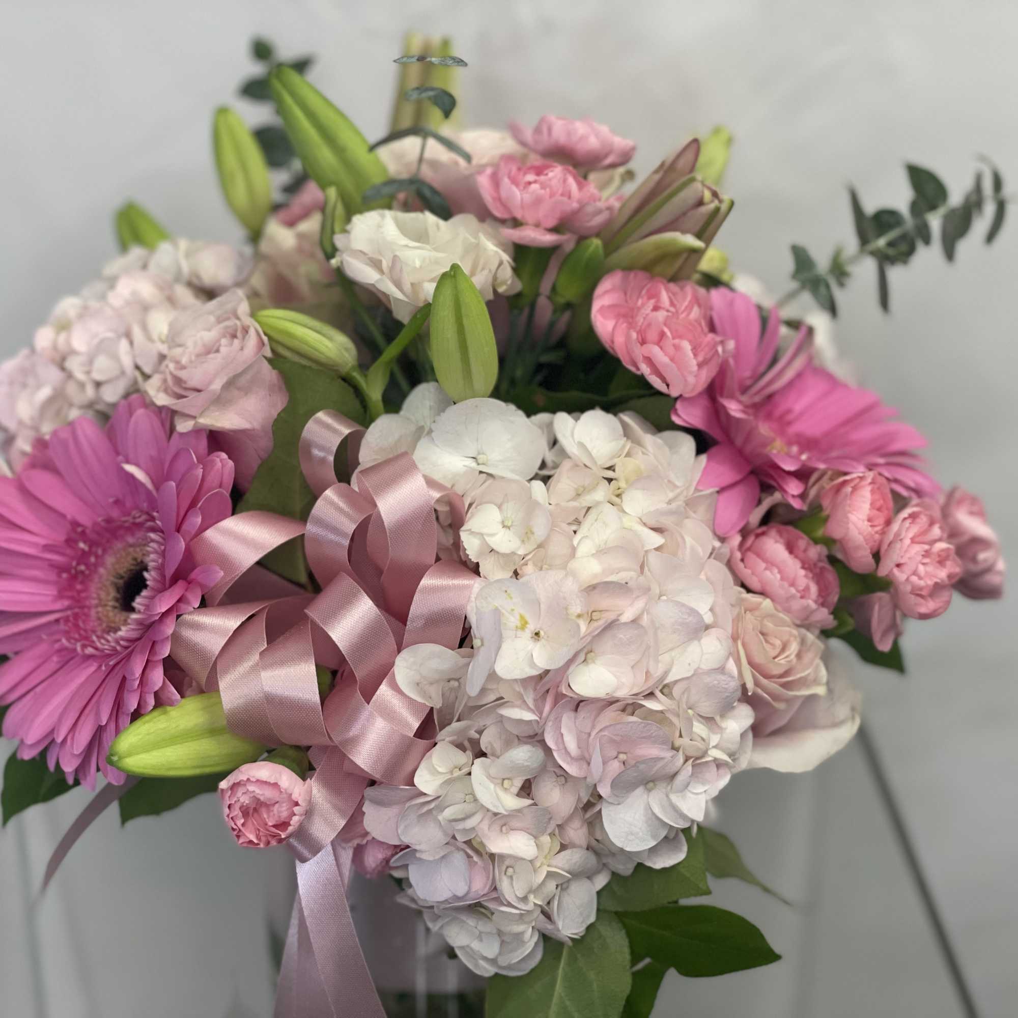 Pink and white bouquet with hydrangeas, lilies, and gerbera daisies tied with a satin ribbon