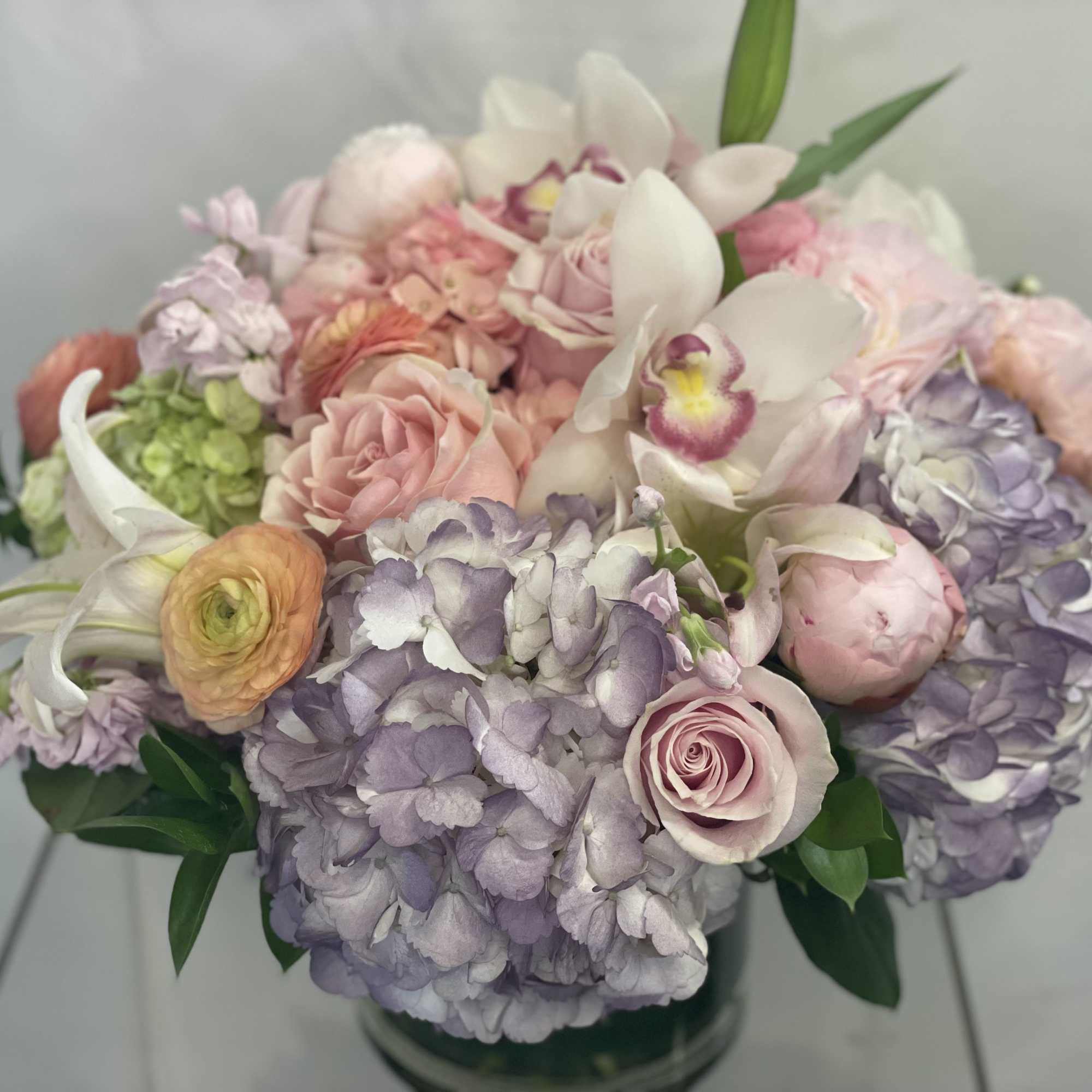 Pastel bouquet with hydrangeas, roses, and orchids in a glass vase