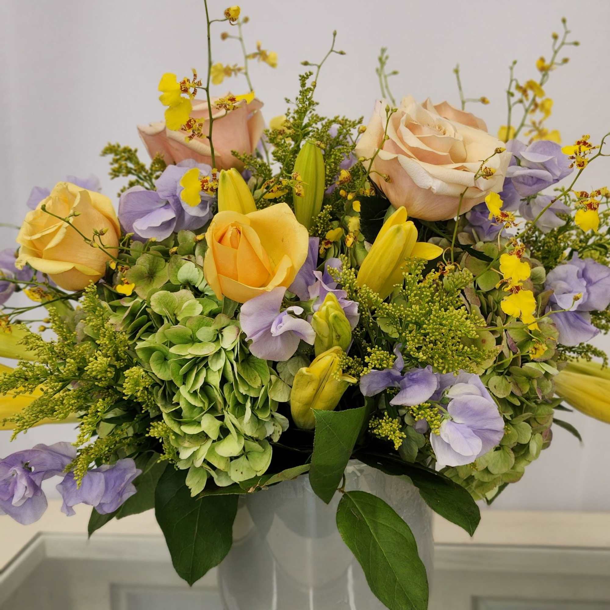 Bouquet of pastel roses, hydrangeas, and yellow orchids in a white vase
