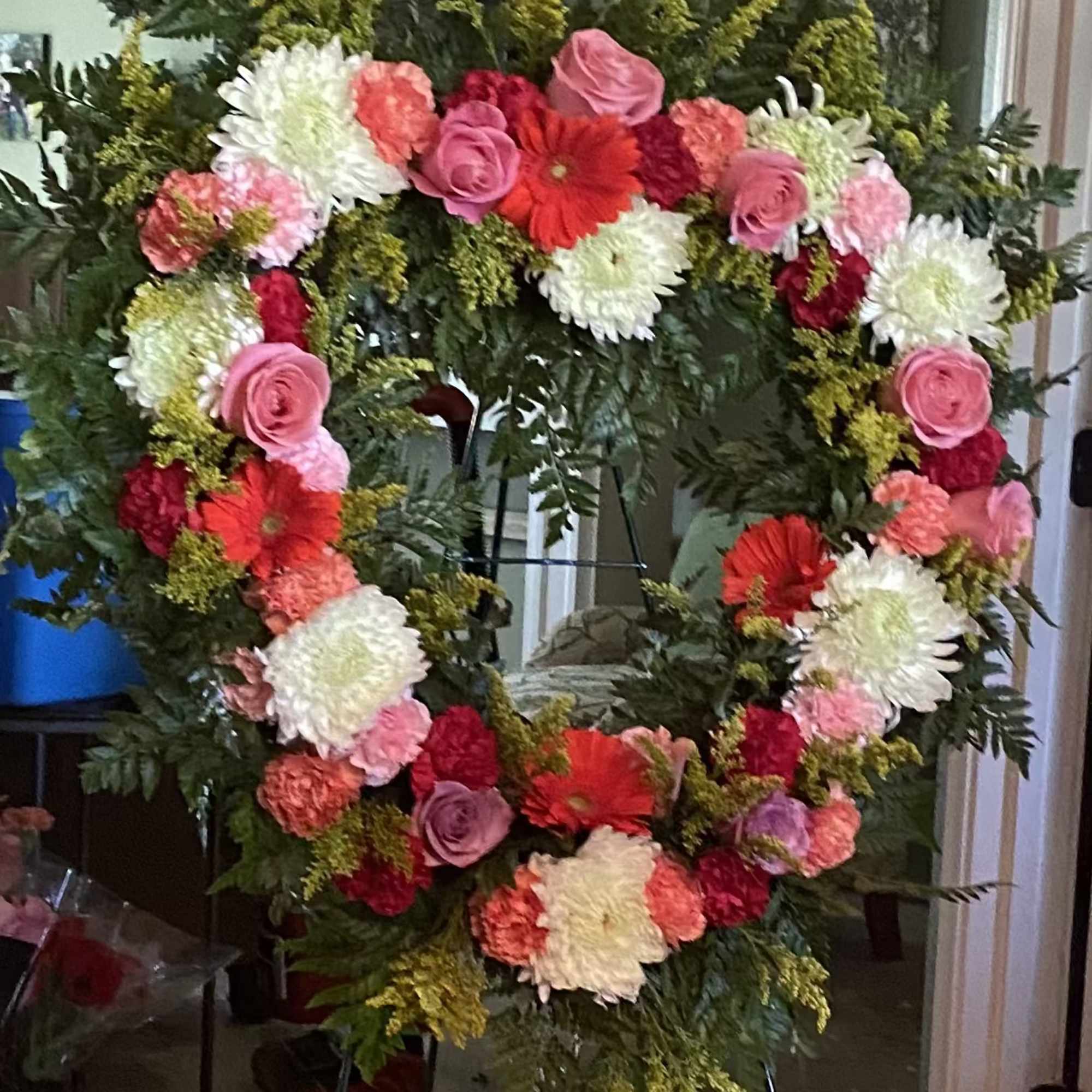 Heart-shaped floral wreath on a stand with pink, red, and white flowers