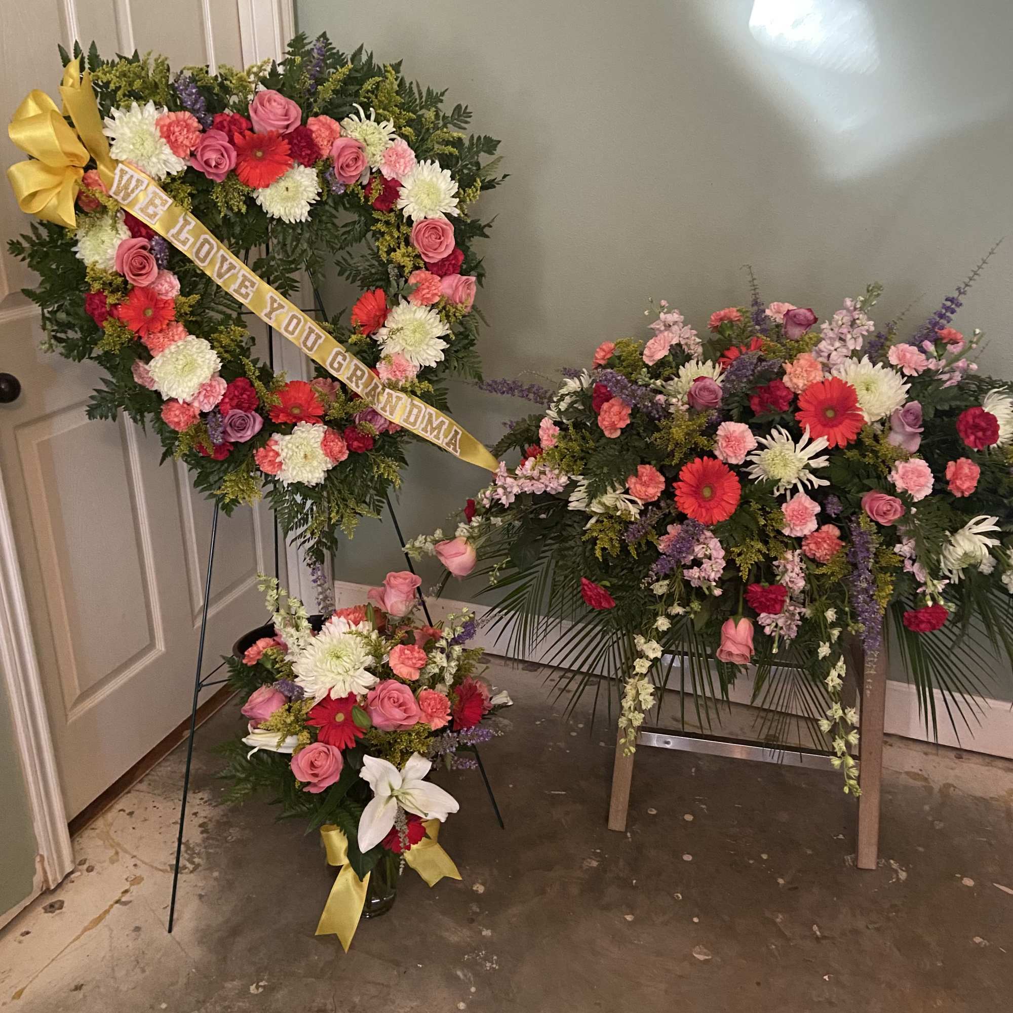 Two floral funeral wreaths and a vase arrangement with pink and white flowers