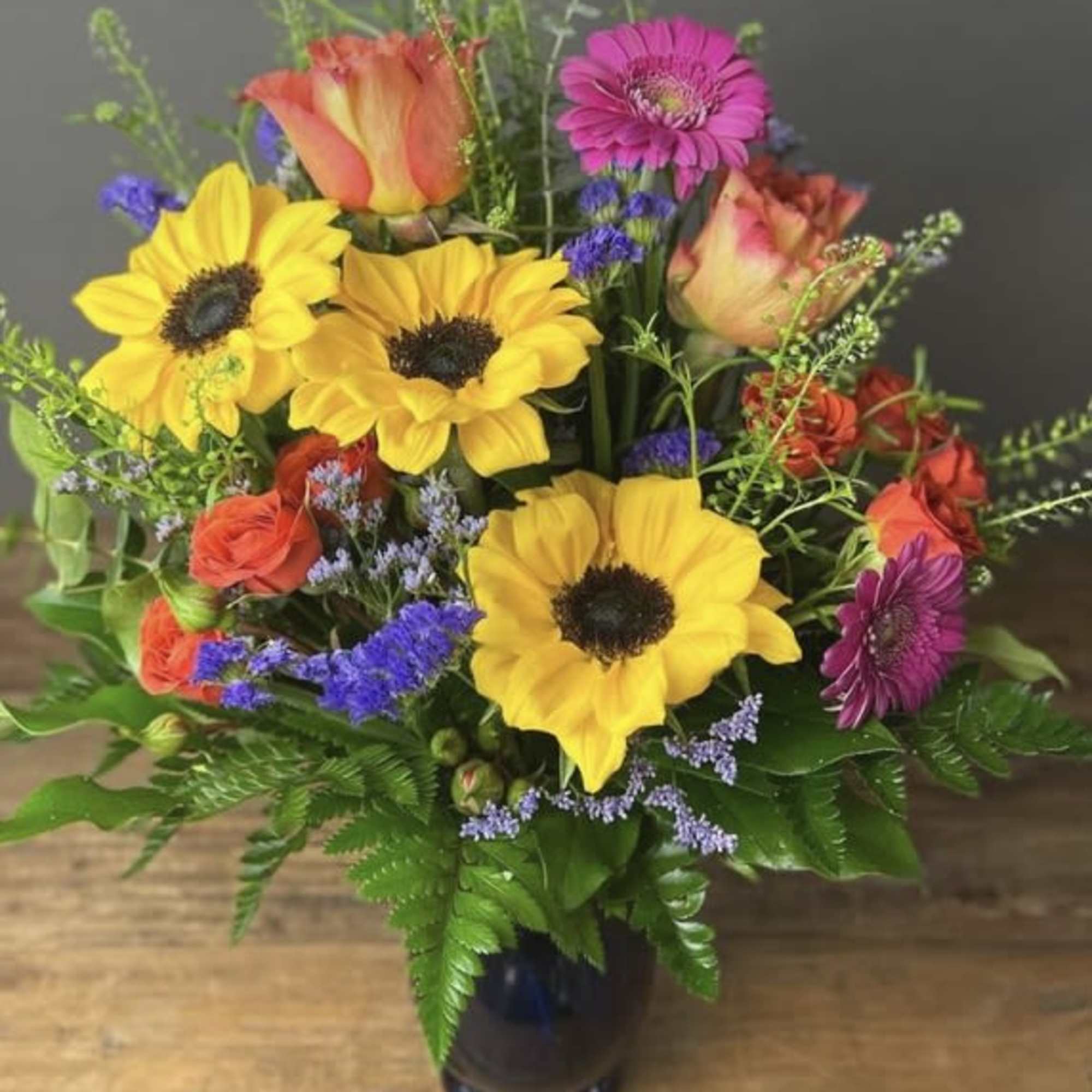 Colorful bouquet of sunflowers, roses, and gerbera daisies in a dark vase