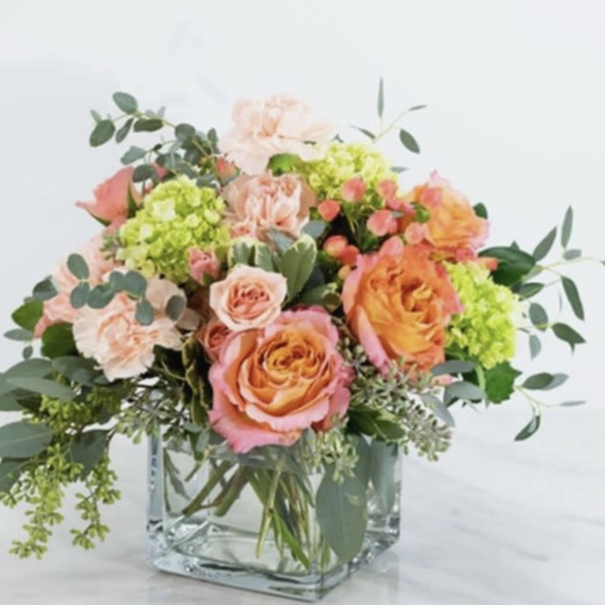 Peach and pink roses in a clear glass vase with green accents