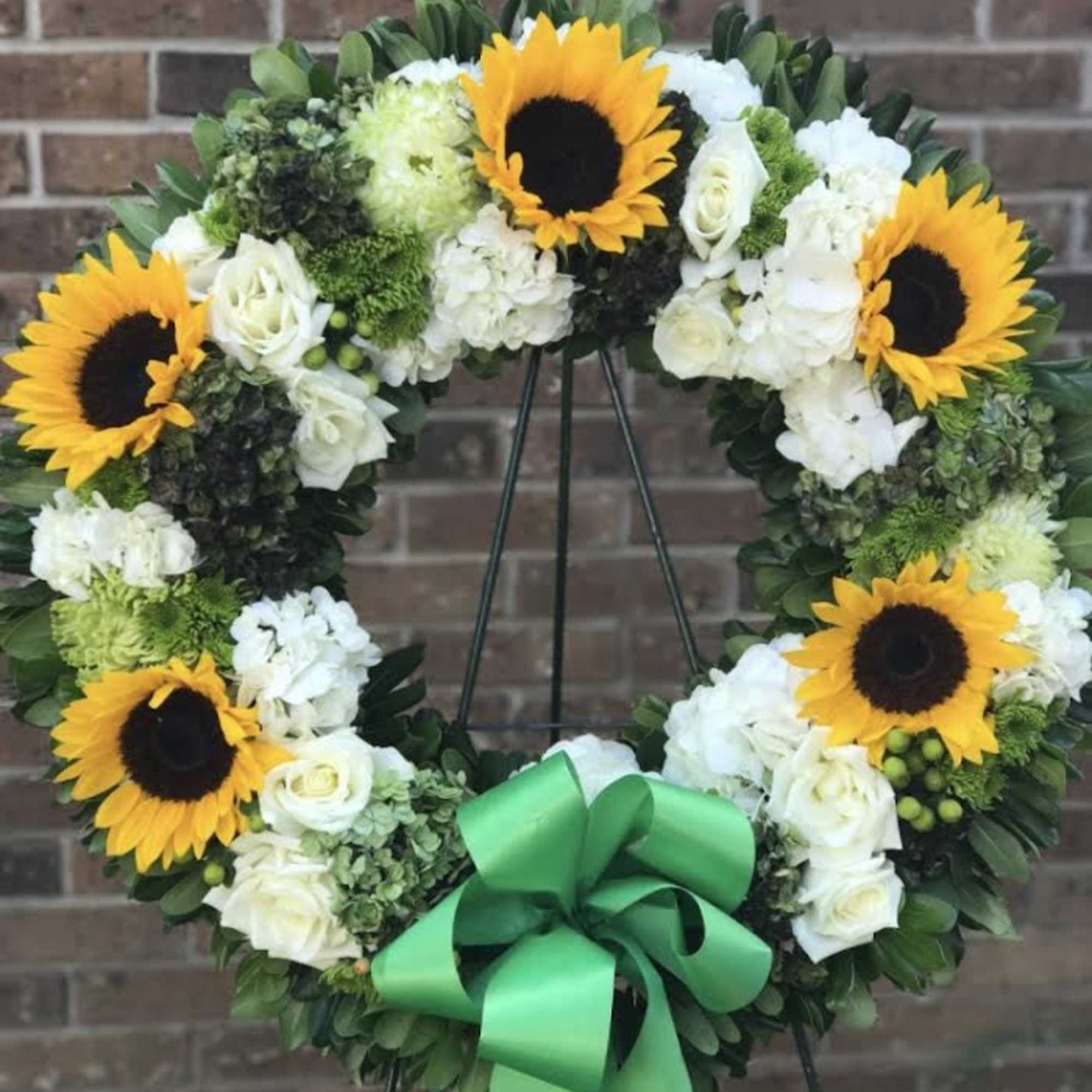 Standing wreath of yellow sunflowers and white flowers with a large green bow