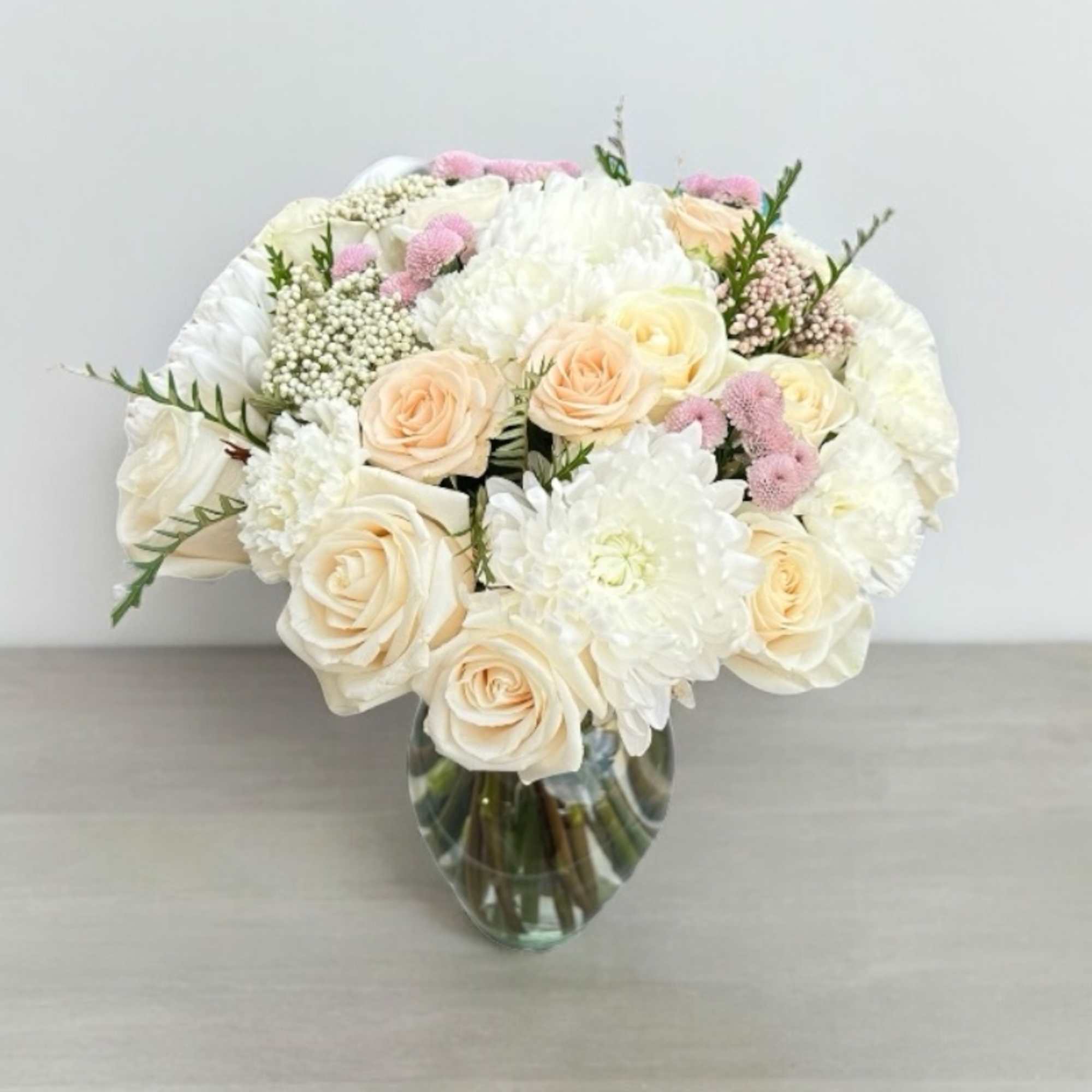 Cream roses and white blooms arranged in a clear glass vase