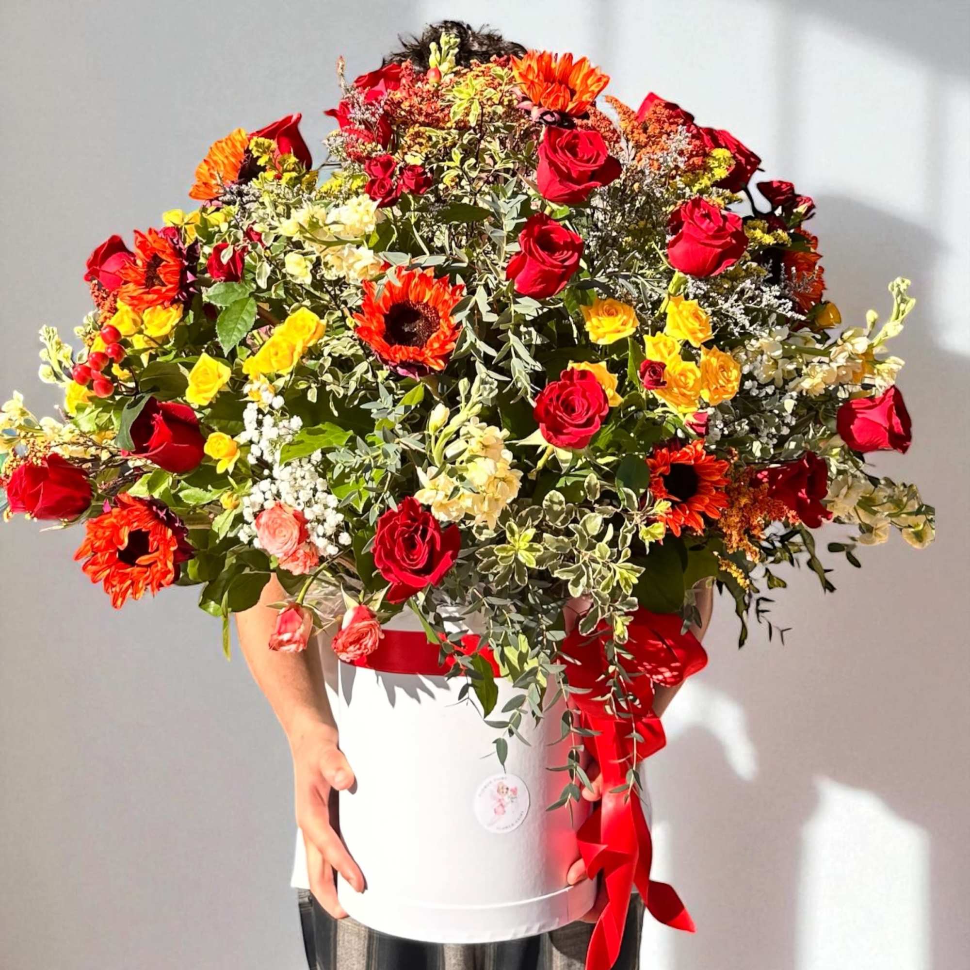 Large mixed bouquet of red, yellow, and orange flowers in a white box with a red ribbon