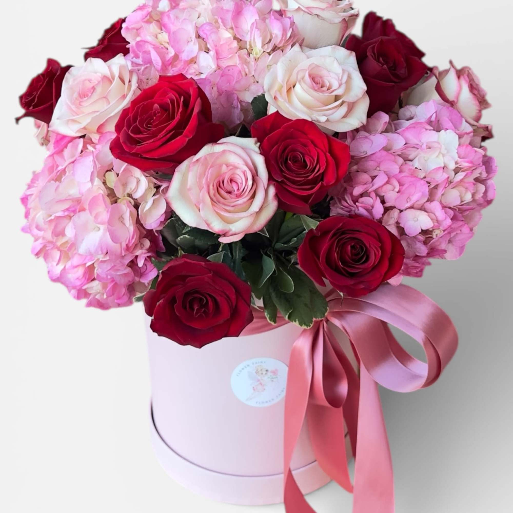 Pink and red roses with hydrangeas in a round pink box tied with ribbon