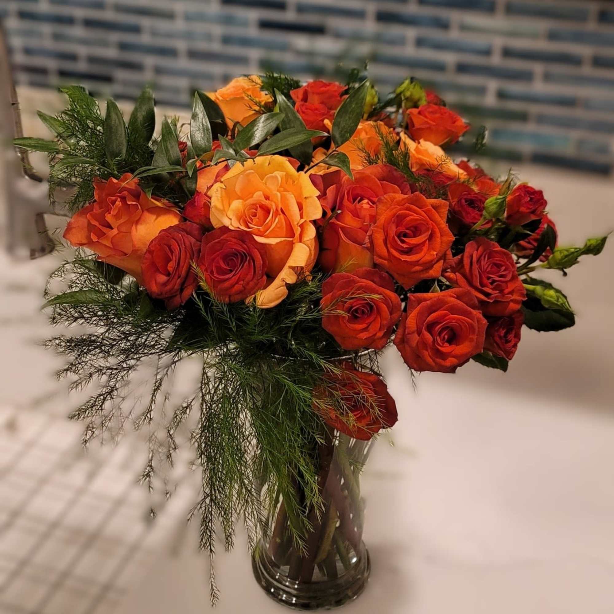 Orange and red roses arranged in a clear glass vase