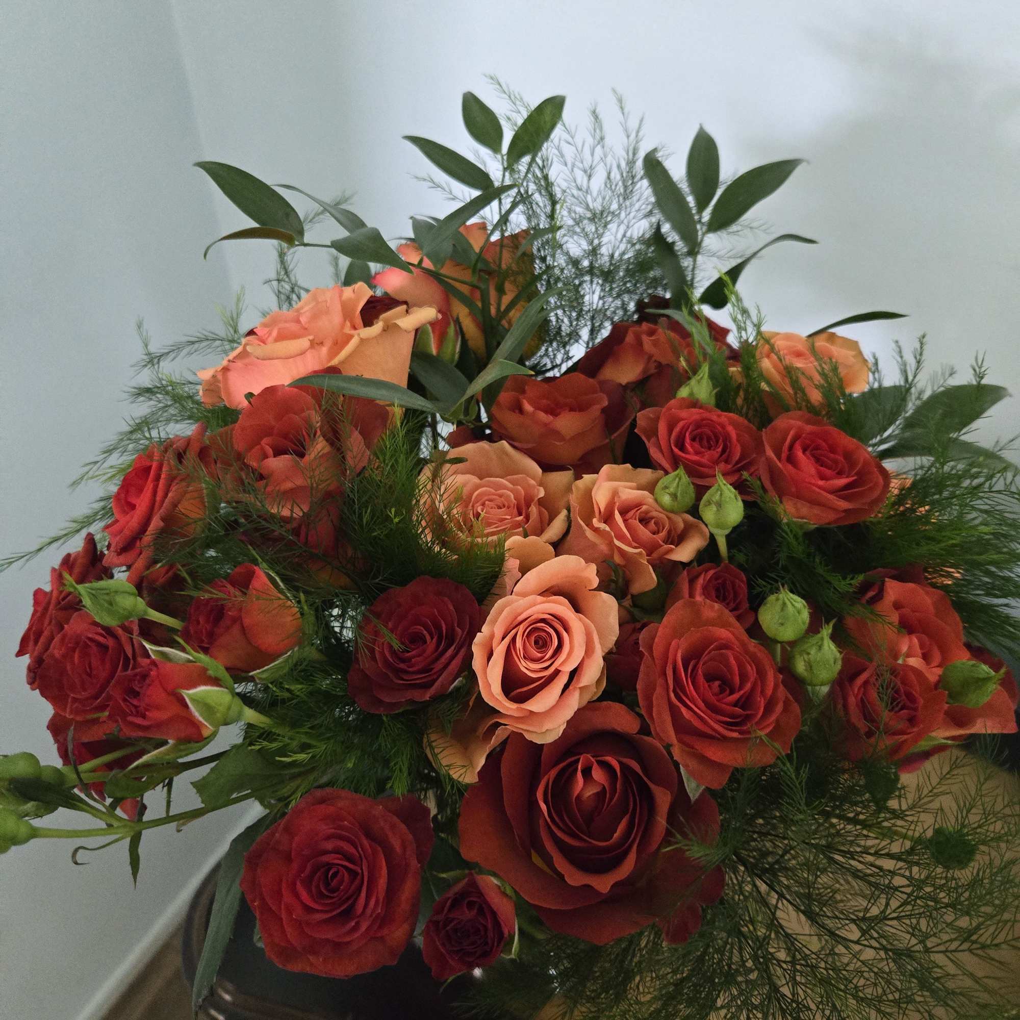 Bouquet of red and peach roses with airy greenery