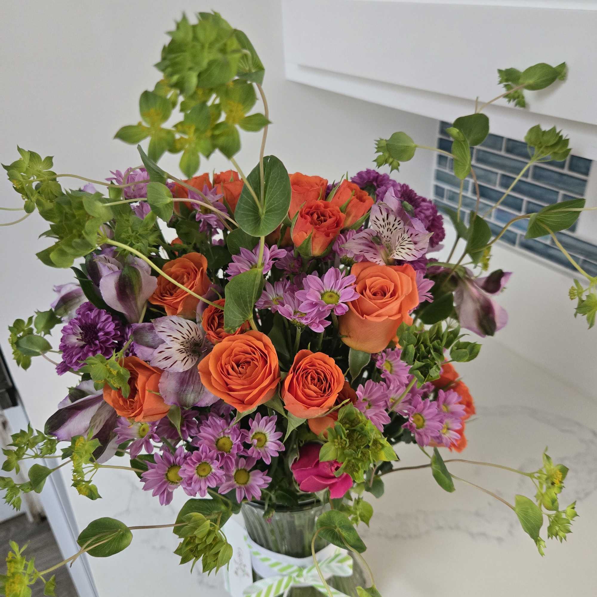 Bouquet of orange roses and purple daisies in a glass vase