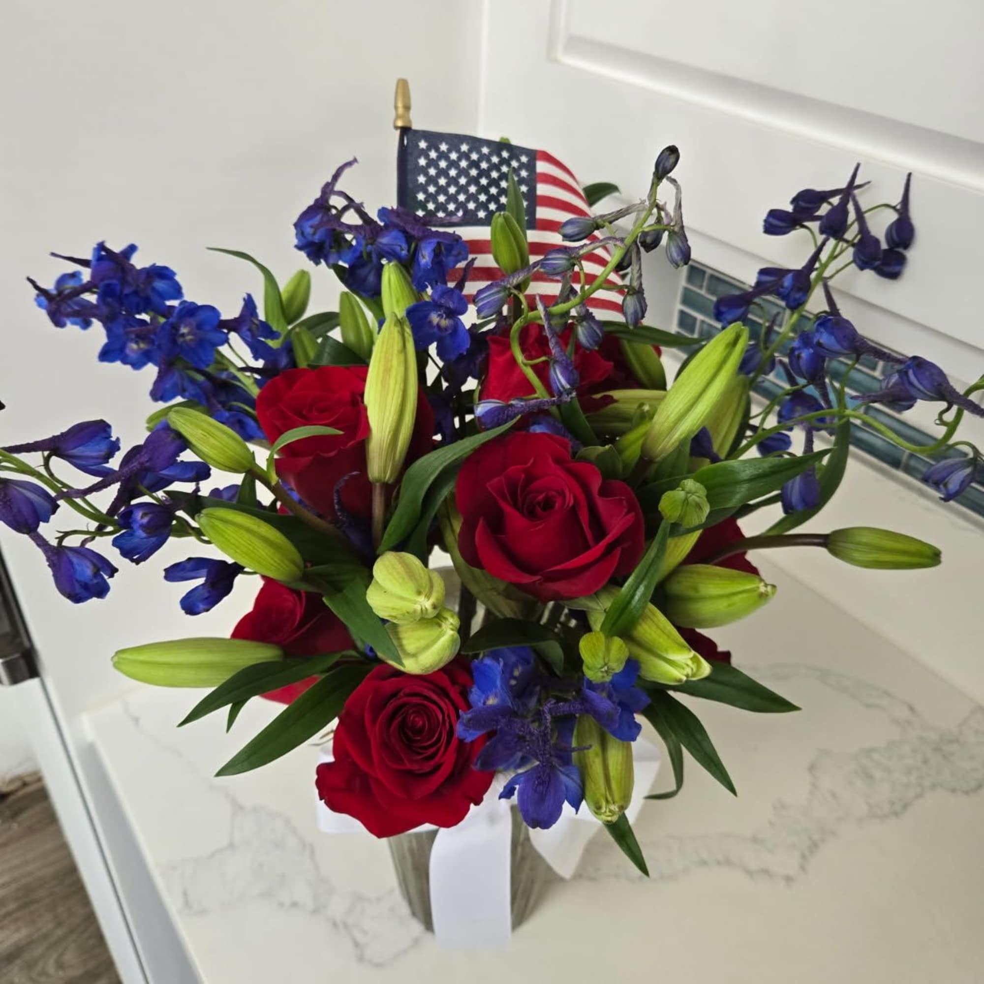 Red roses and blue flowers in a clear vase with an American flag