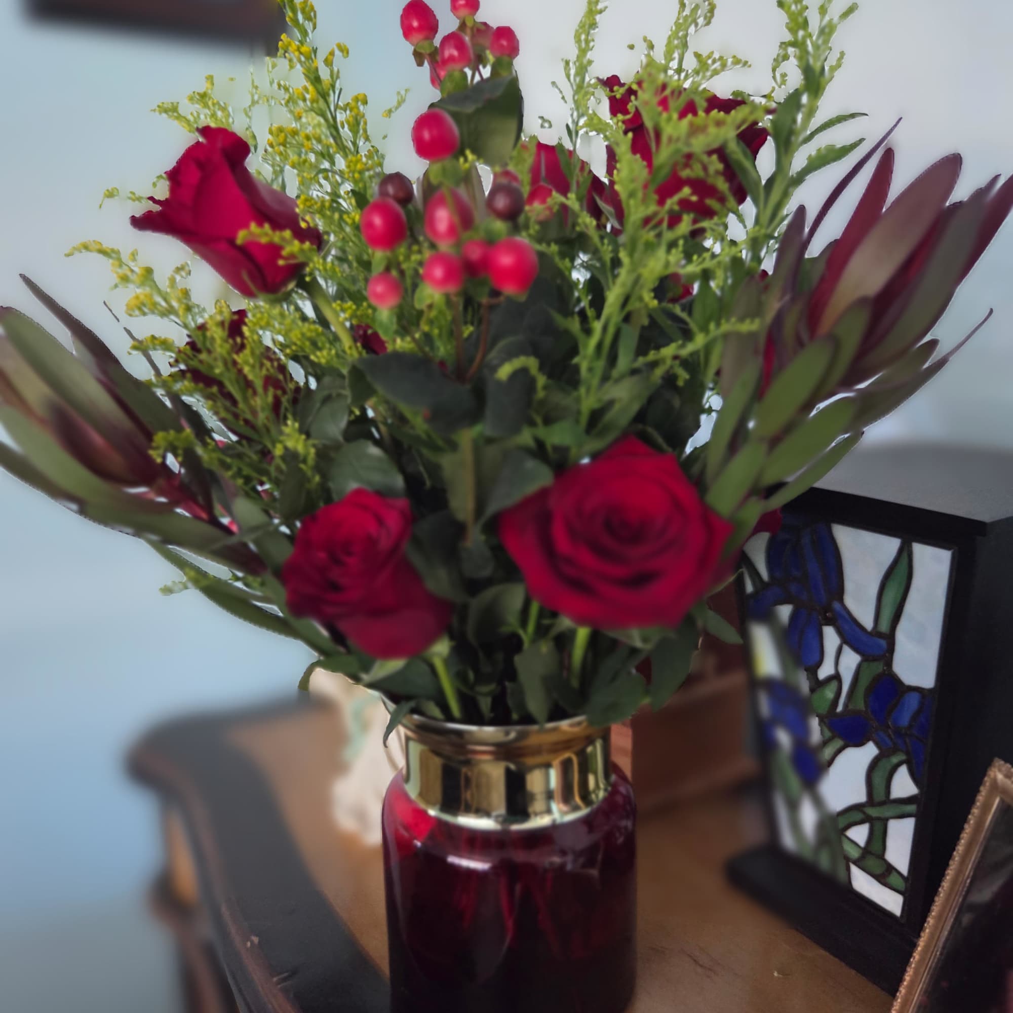 Red roses and berry stems arranged in a glass vase