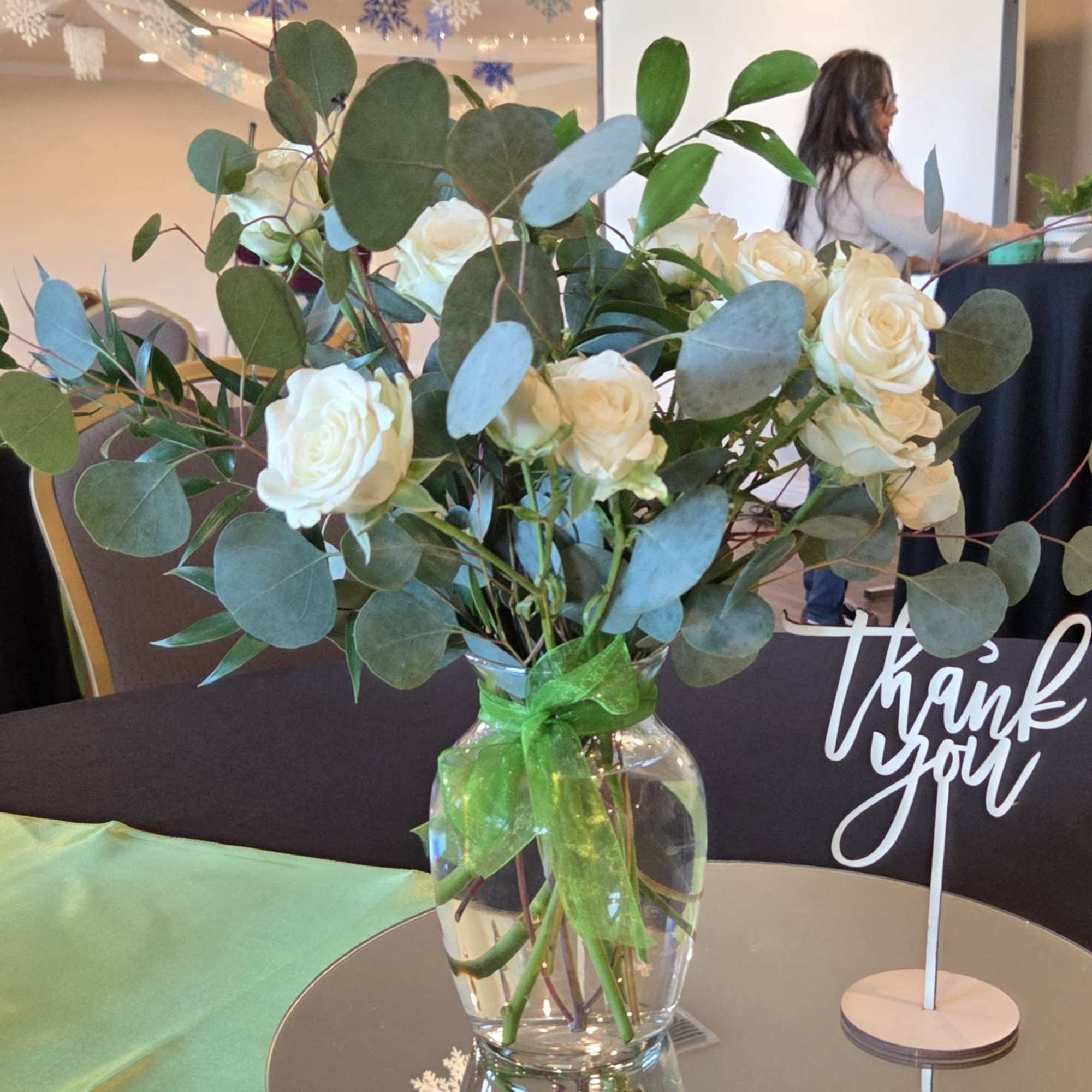 White roses in a clear glass vase with eucalyptus and a green ribbon