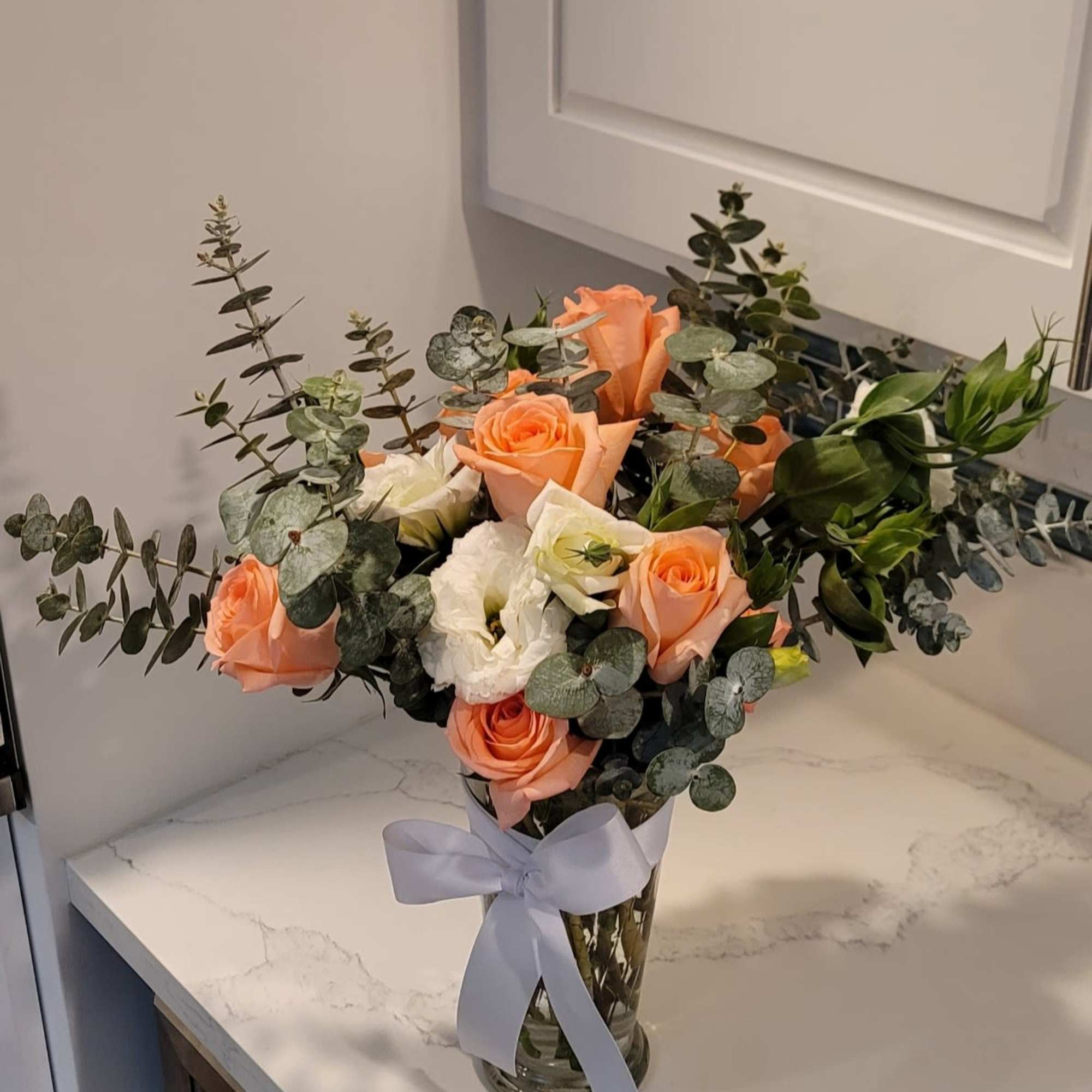 Peach and white roses arranged in a clear glass vase with a ribbon.
