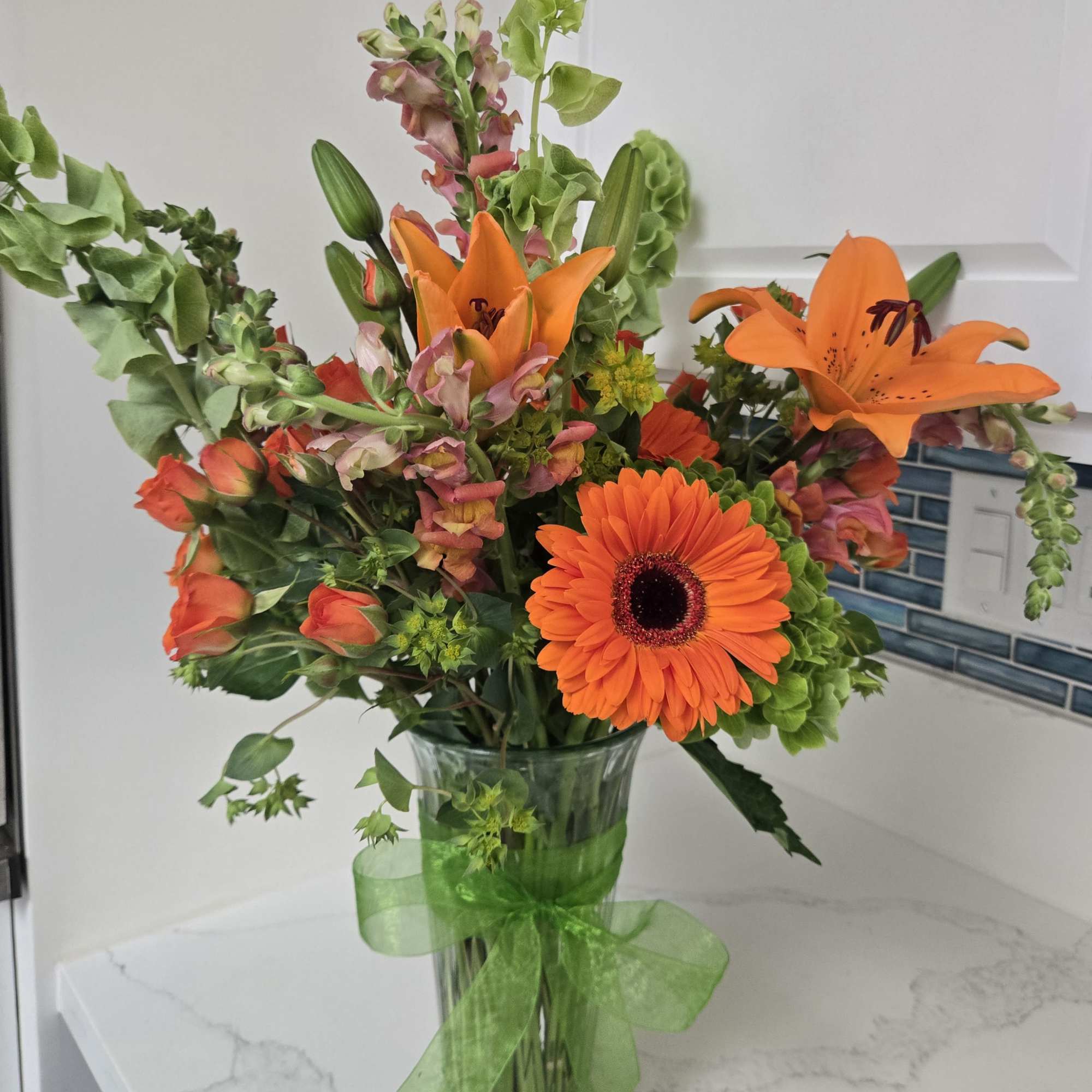 Orange mixed bouquet in a clear glass vase with a green ribbon