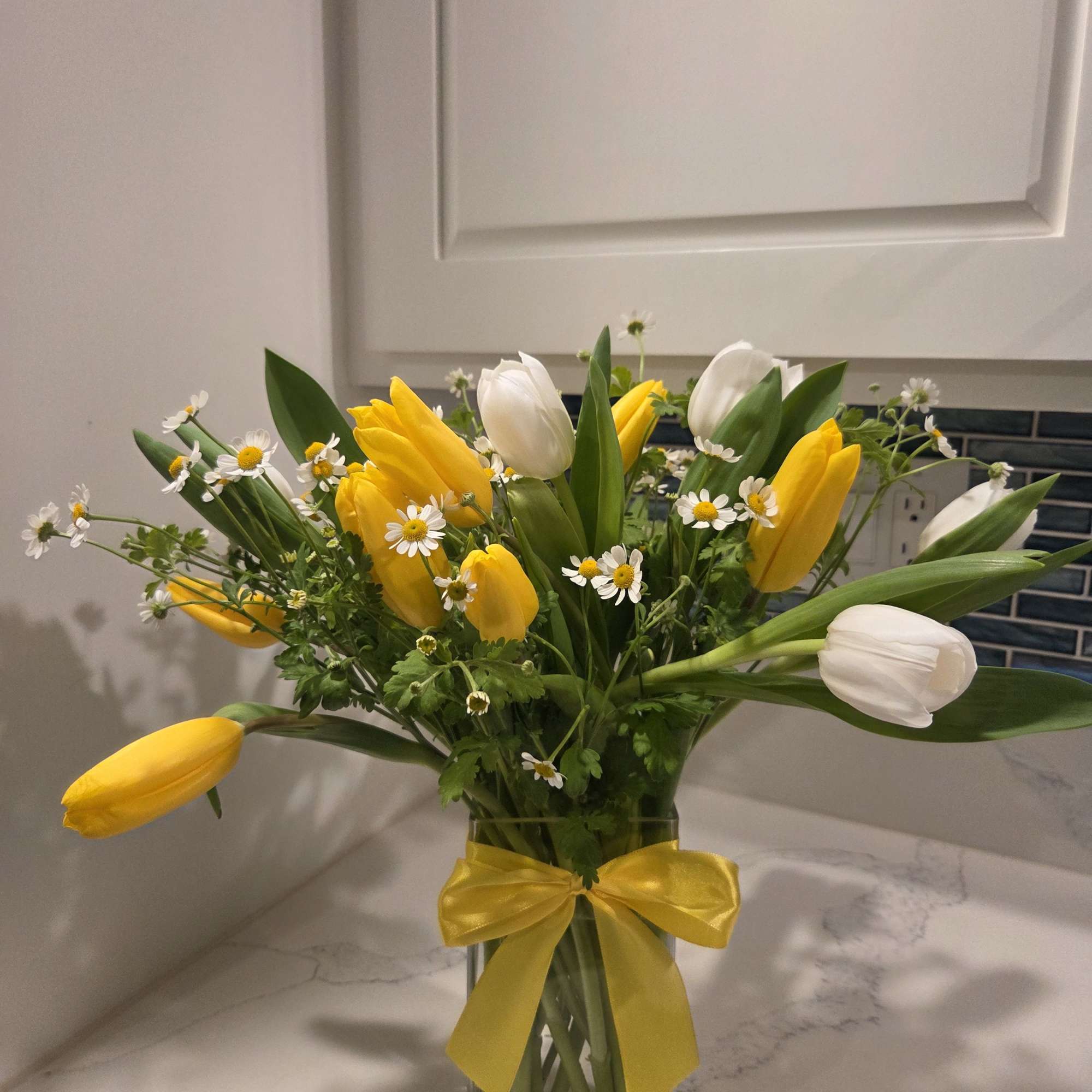 Yellow and white tulips with small daisies in a glass vase