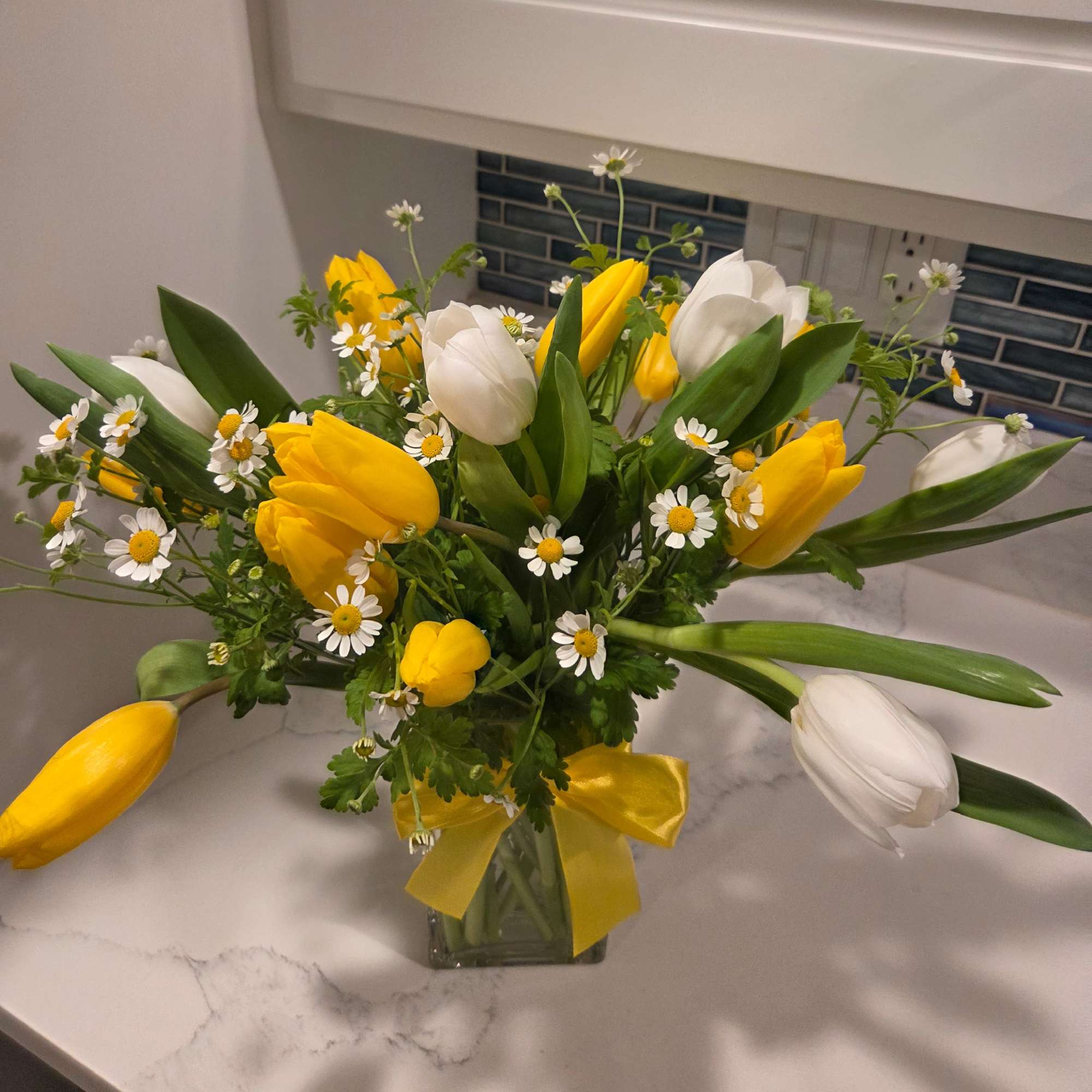 Yellow and white tulips with small white daisies in a glass vase