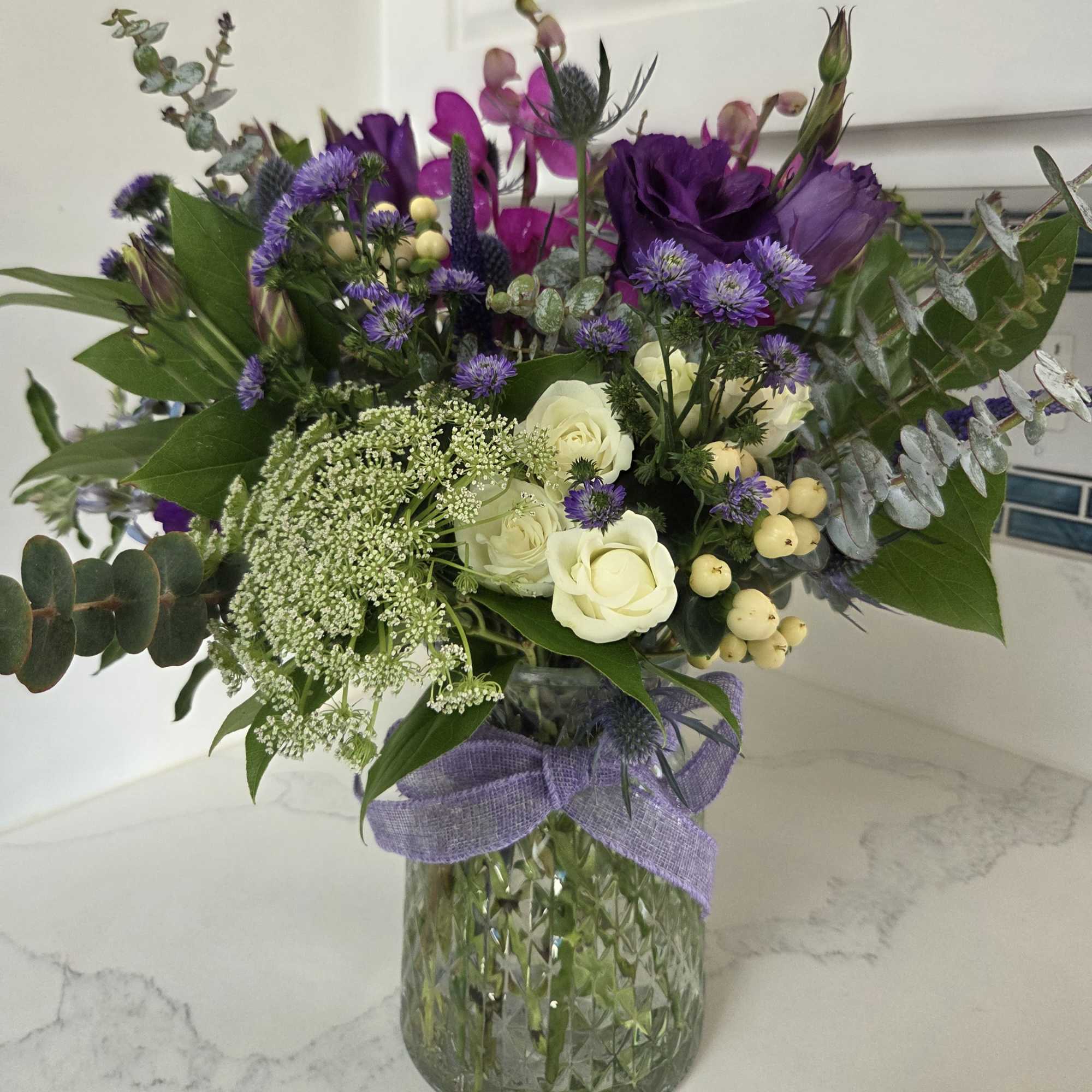 This floral arrangement features rich, moody shades of blue, purple and green