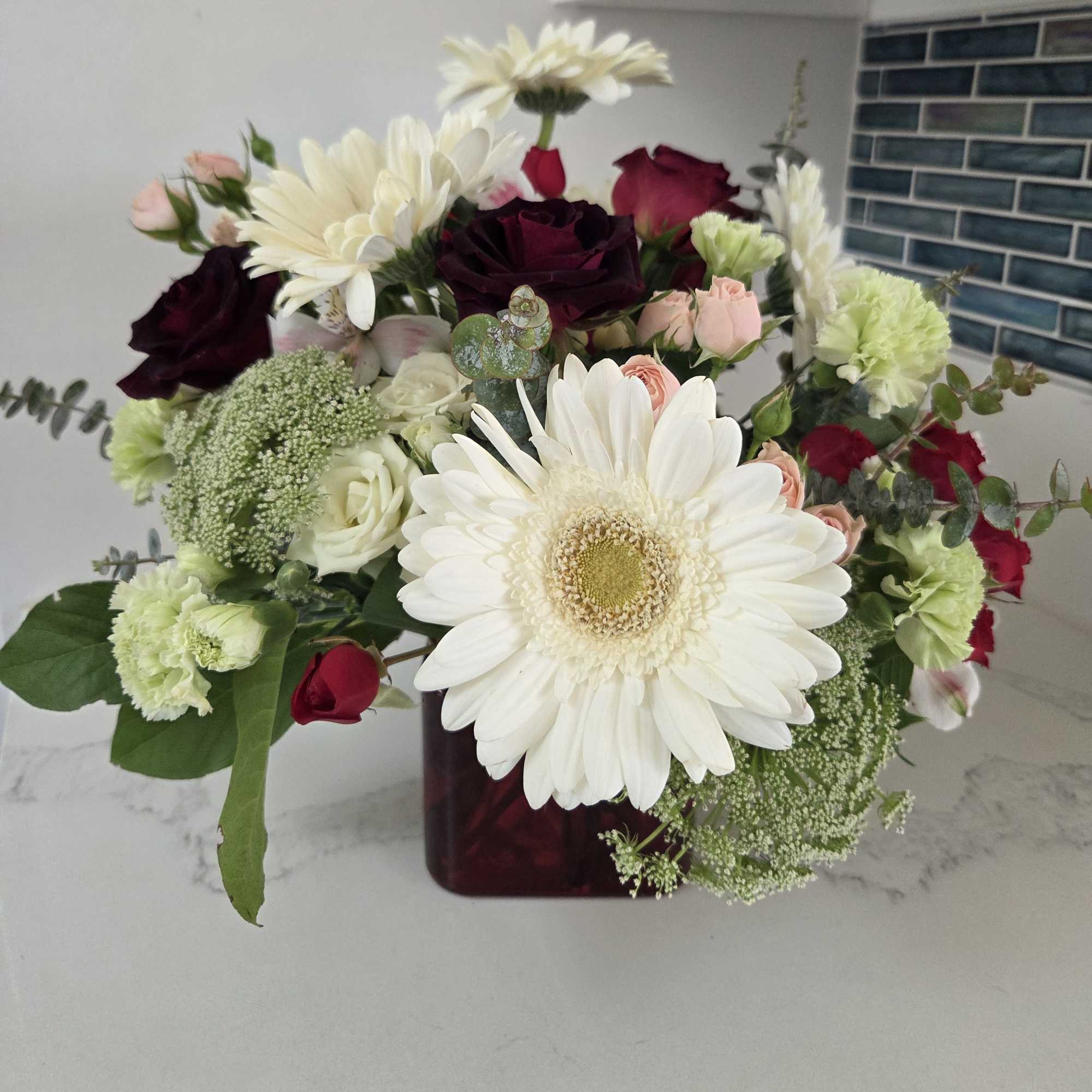 Mixed bouquet of white daisies, roses, and pink spray roses in a dark vase