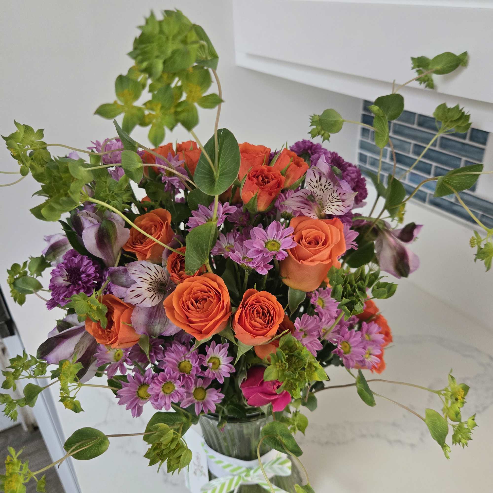 Bouquet of orange roses and purple flowers in a glass vase