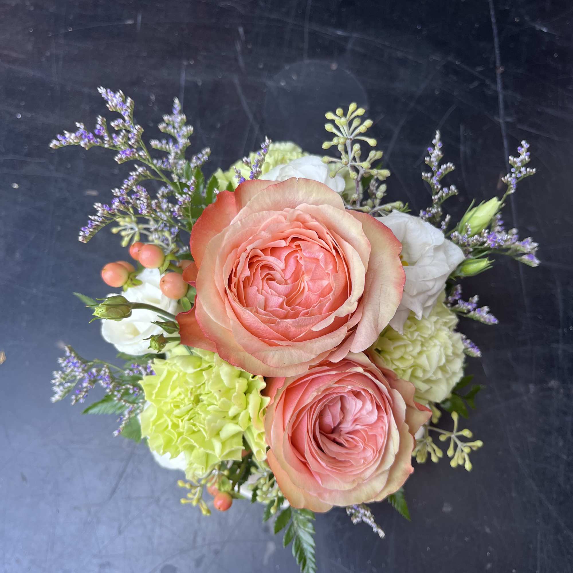Pink roses with white blooms and green carnations in a small bouquet
