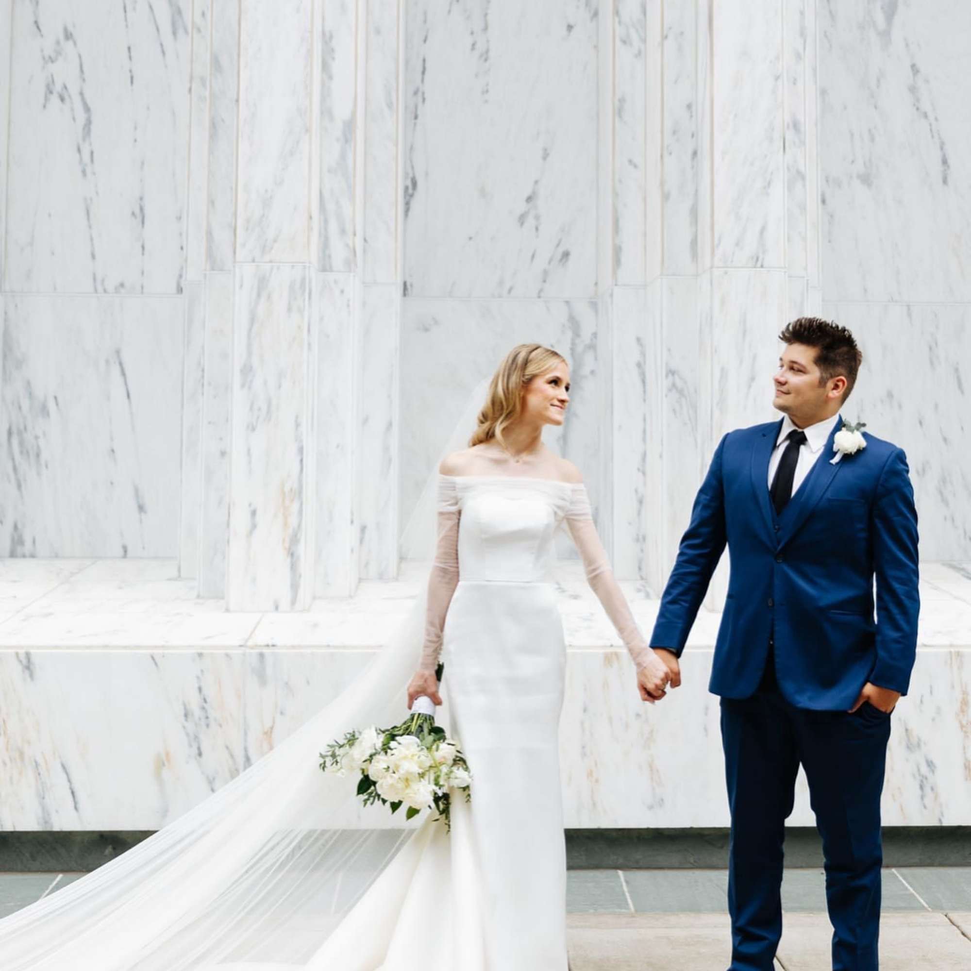 Bride holding a white bouquet beside a groom in a blue suit