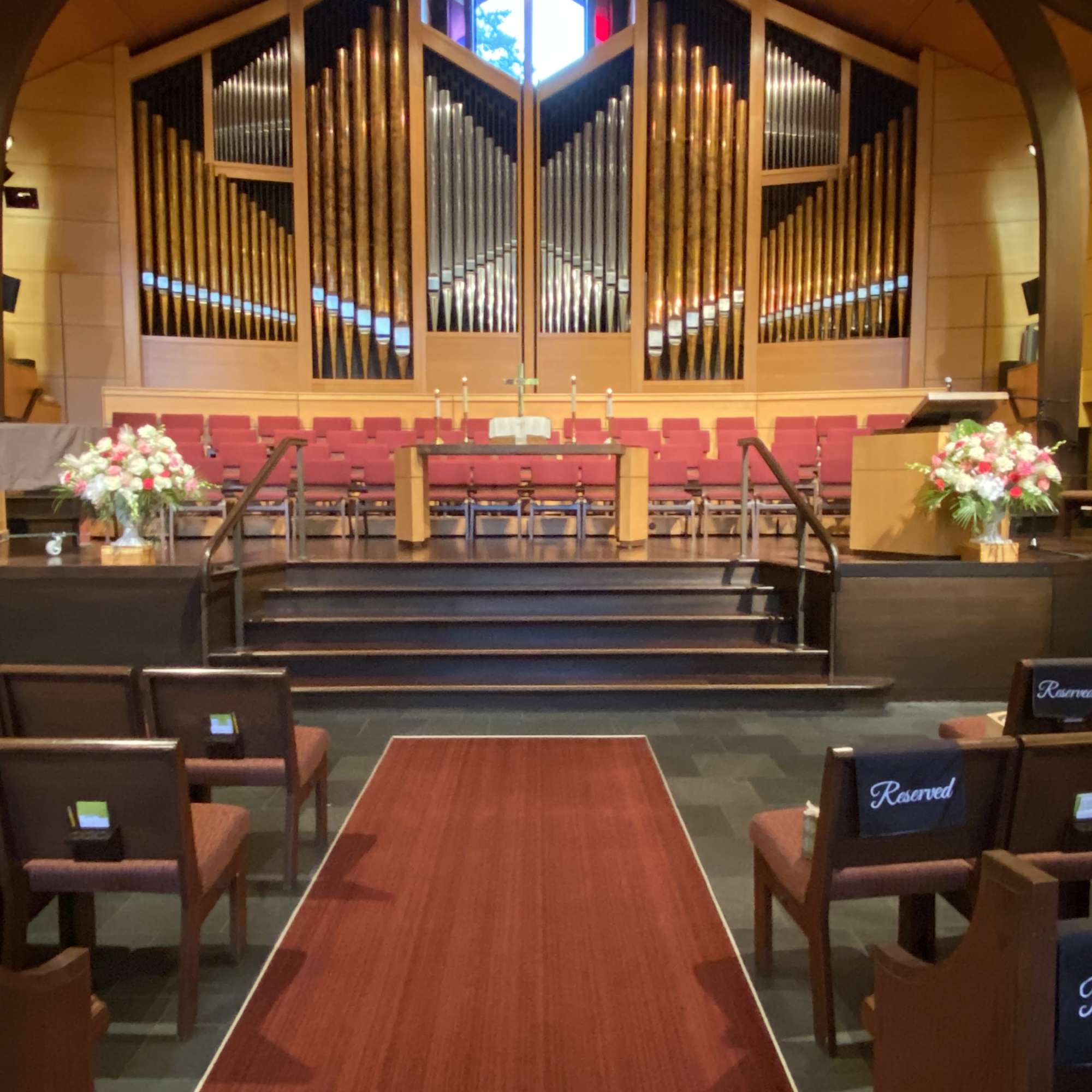 Church sanctuary with floral arrangements flanking the altar and a red aisle runner