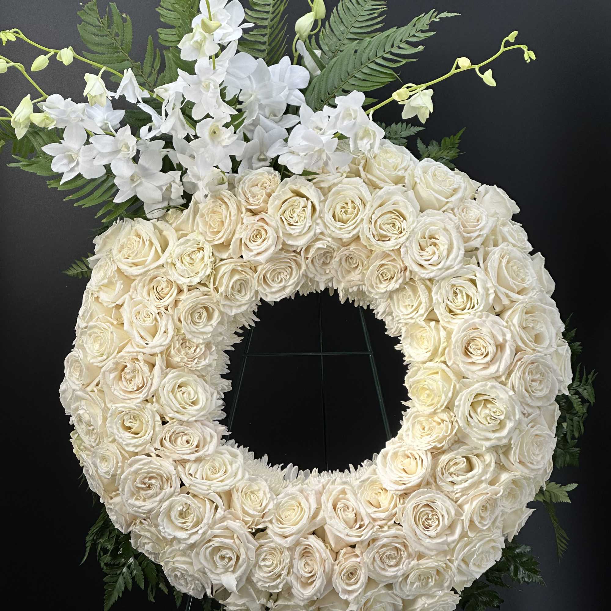 A full, circular sympathy wreath centered on creamy white roses creates an