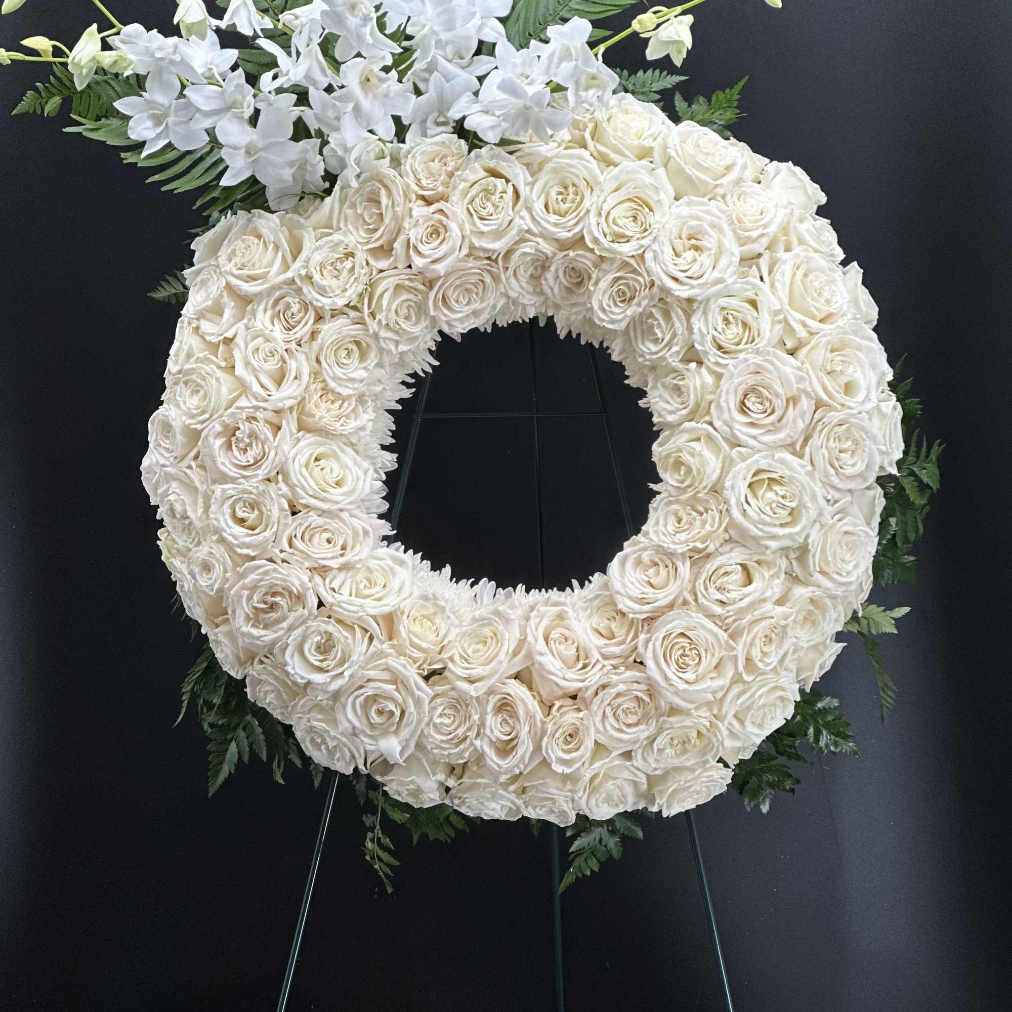 A full, circular sympathy wreath centered on creamy white roses creates an