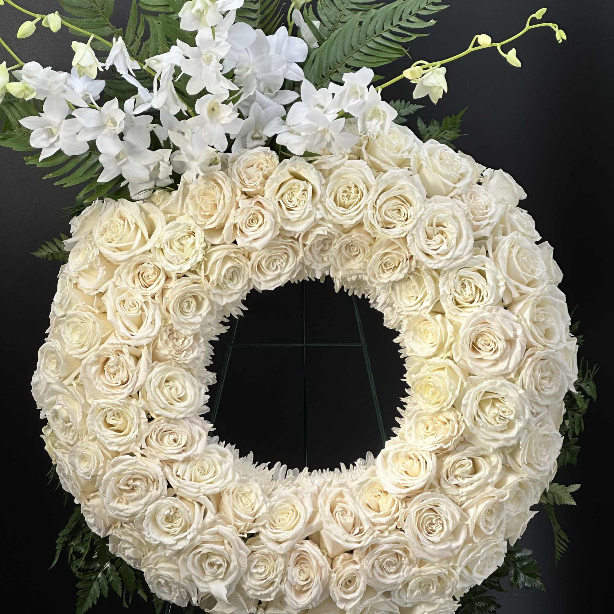 A full, circular sympathy wreath centered on creamy white roses creates an