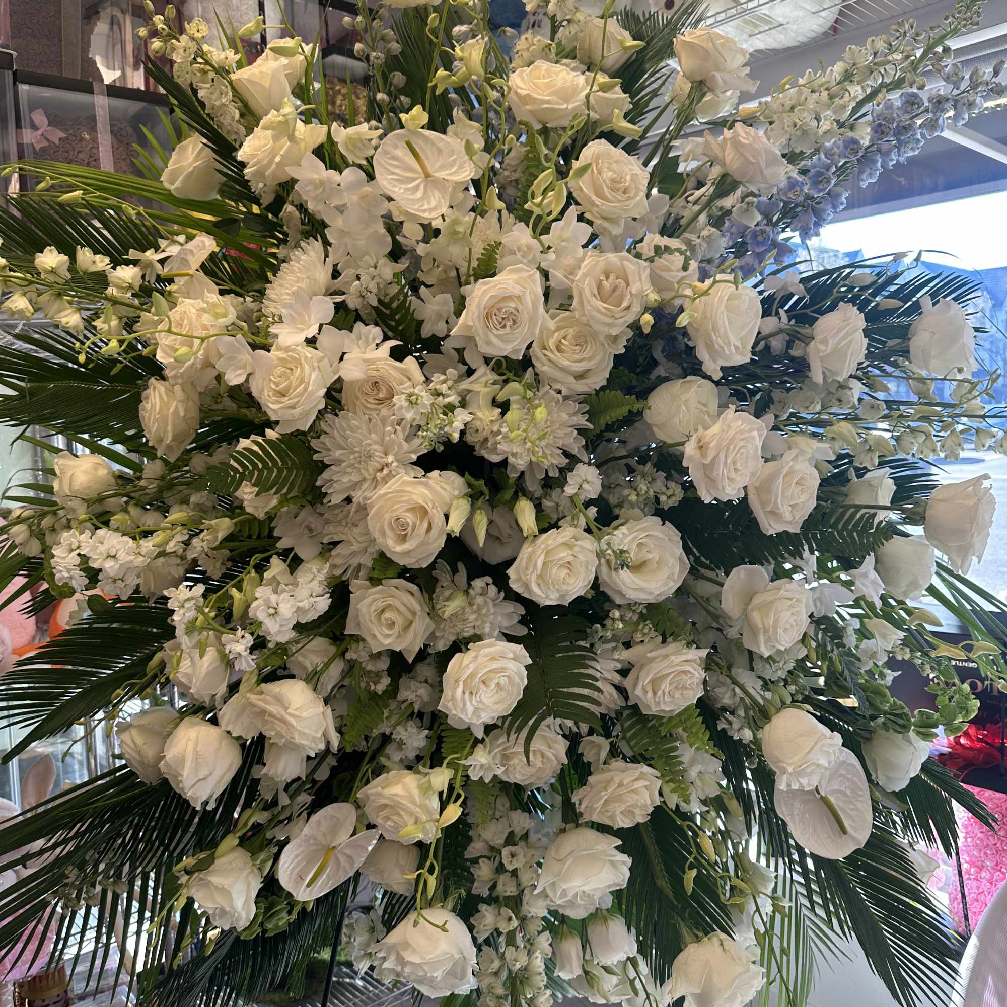 Large standing spray of white roses and other white flowers with cascading blooms and palm fronds on a metal easel