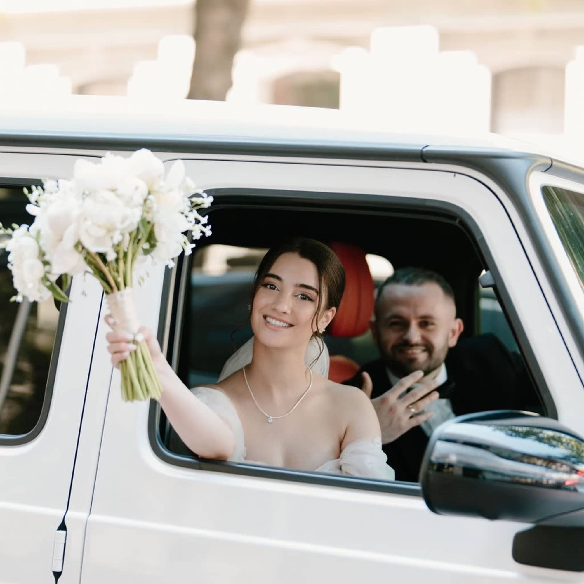 Bride holding a white bouquet from a car window