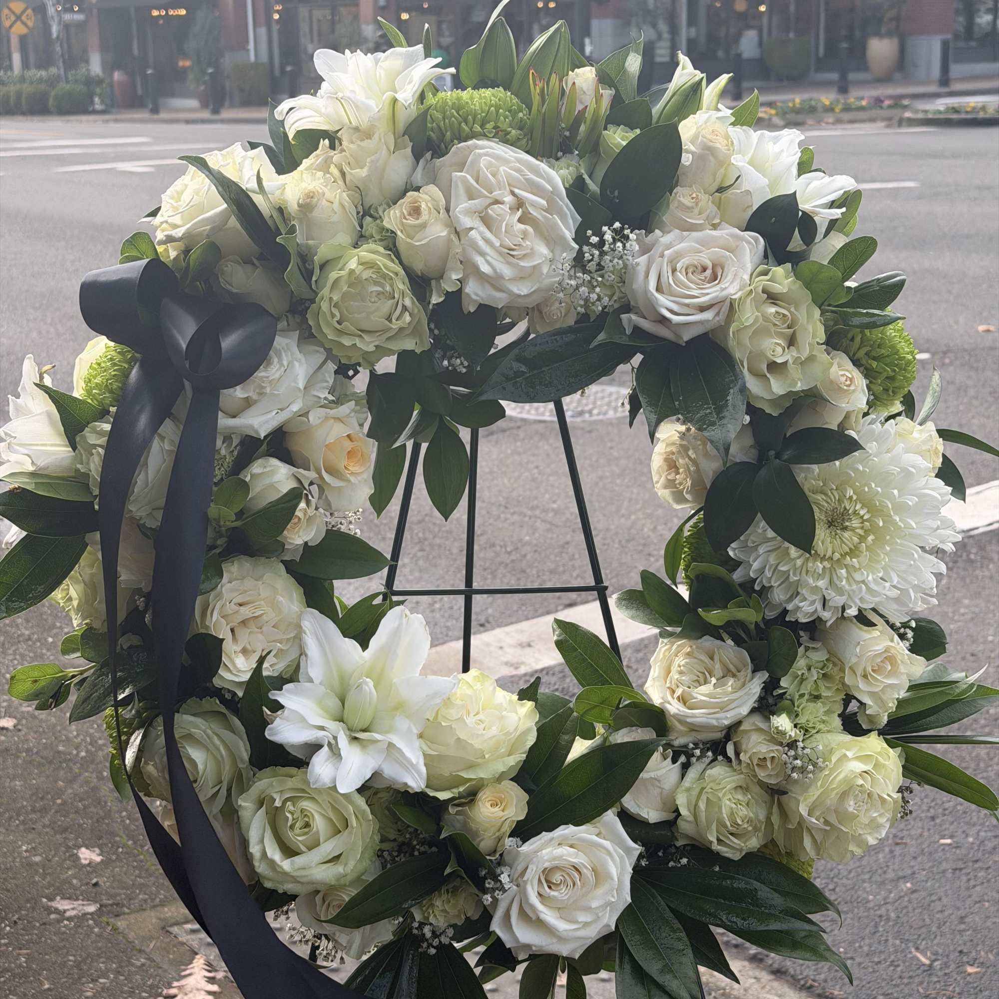 A full, circular sympathy wreath centered on creamy white roses creates an