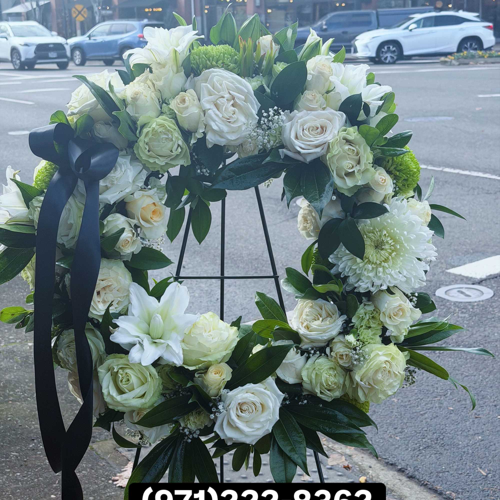 A full, circular sympathy wreath centered on creamy white roses creates an