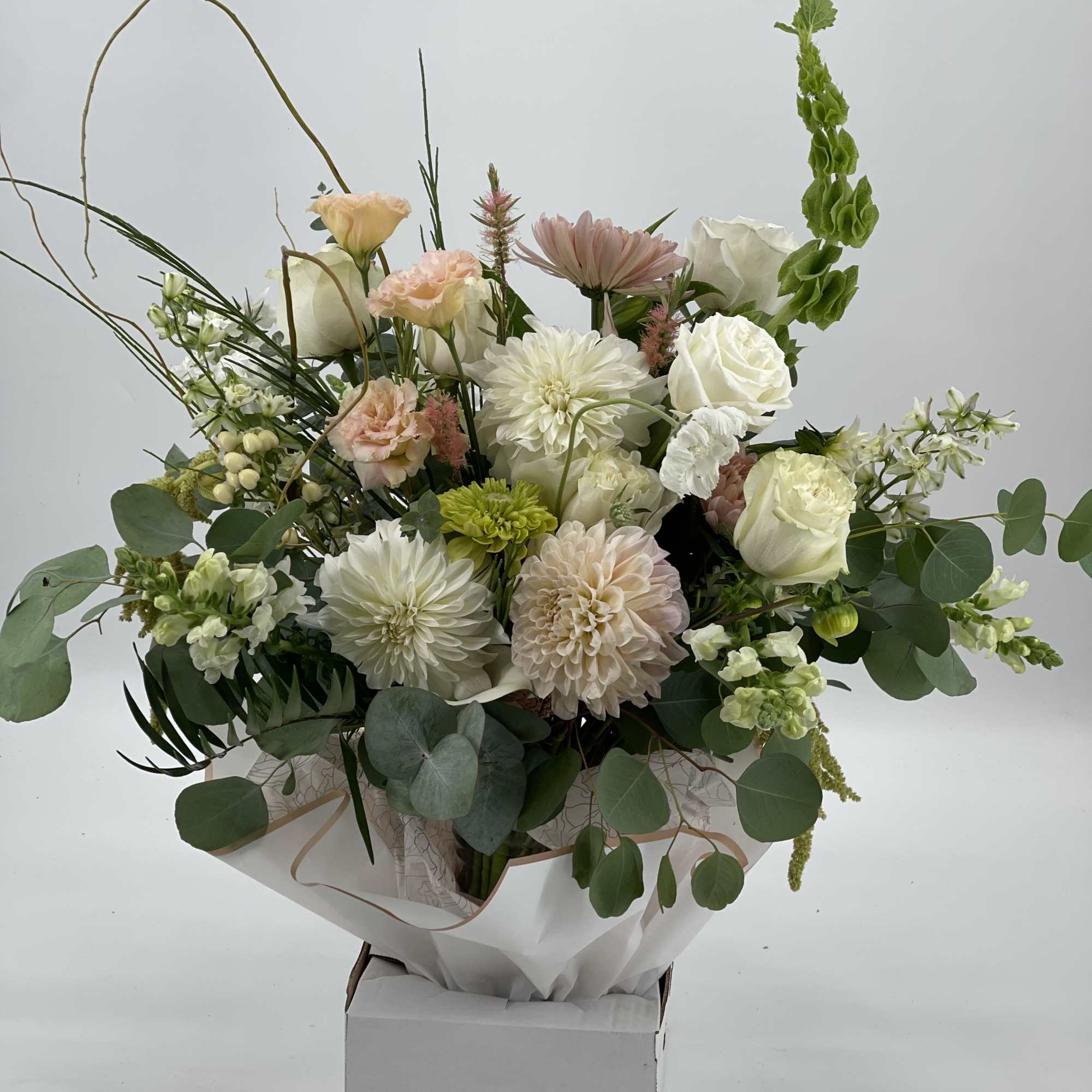 Mixed bouquet of white, blush, and green flowers in a box