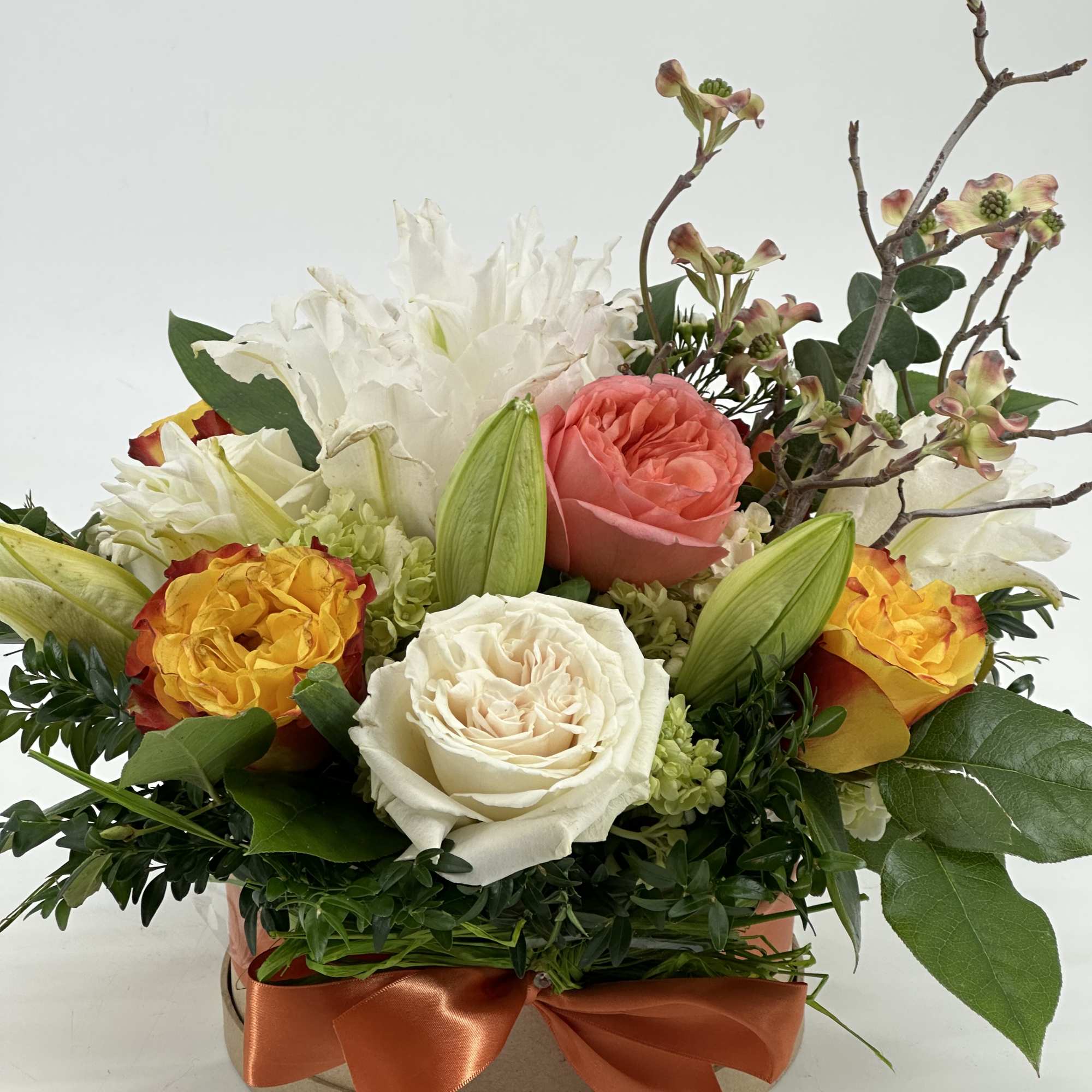 Mixed roses and white lilies in a round box with an orange ribbon