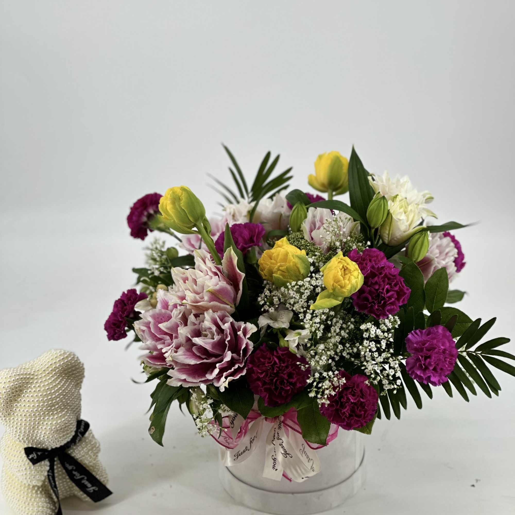 Bouquet of pink, white, and yellow flowers in a clear round box with a small teddy bear