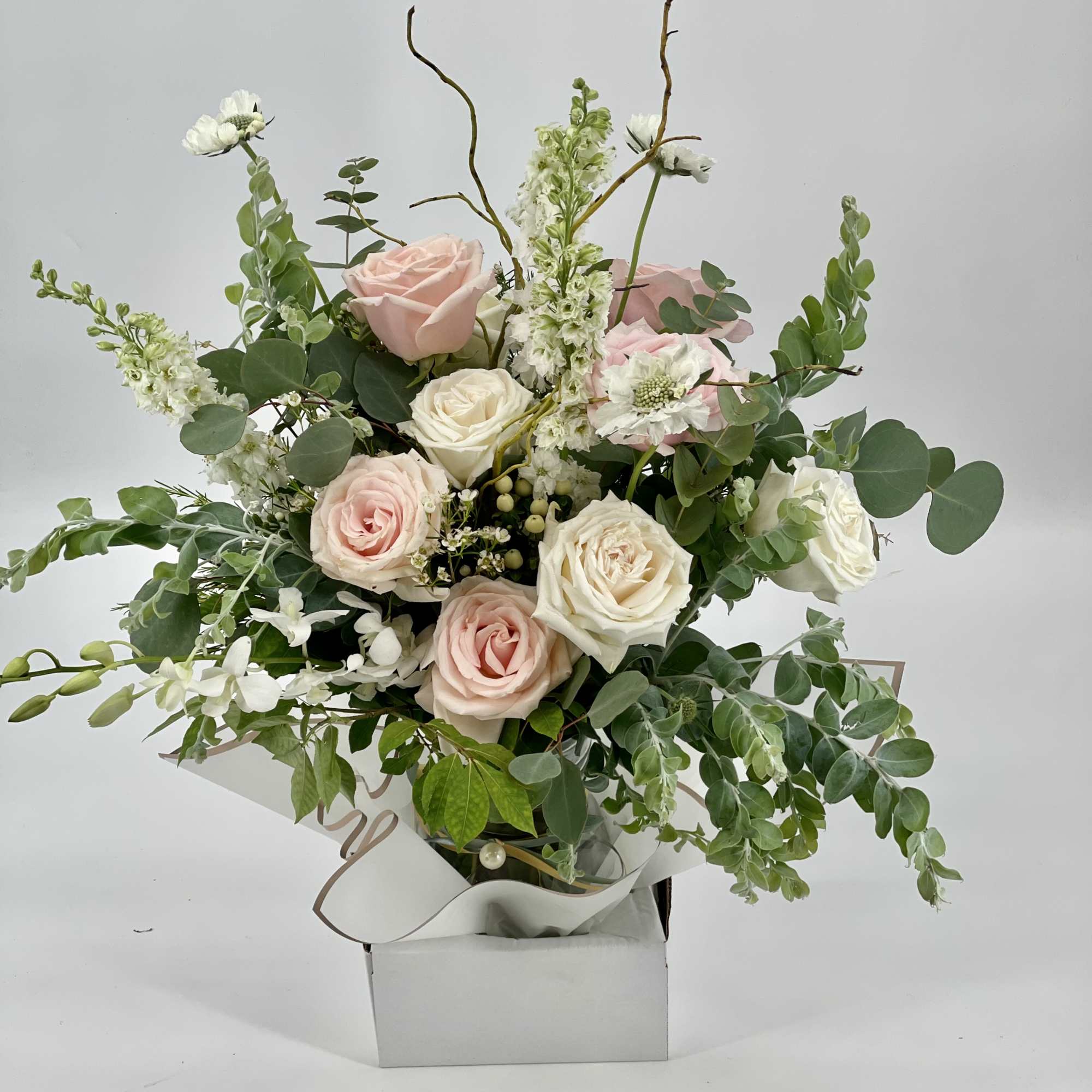 Pastel arrangement of pink and cream roses with white accent flowers in a white box container