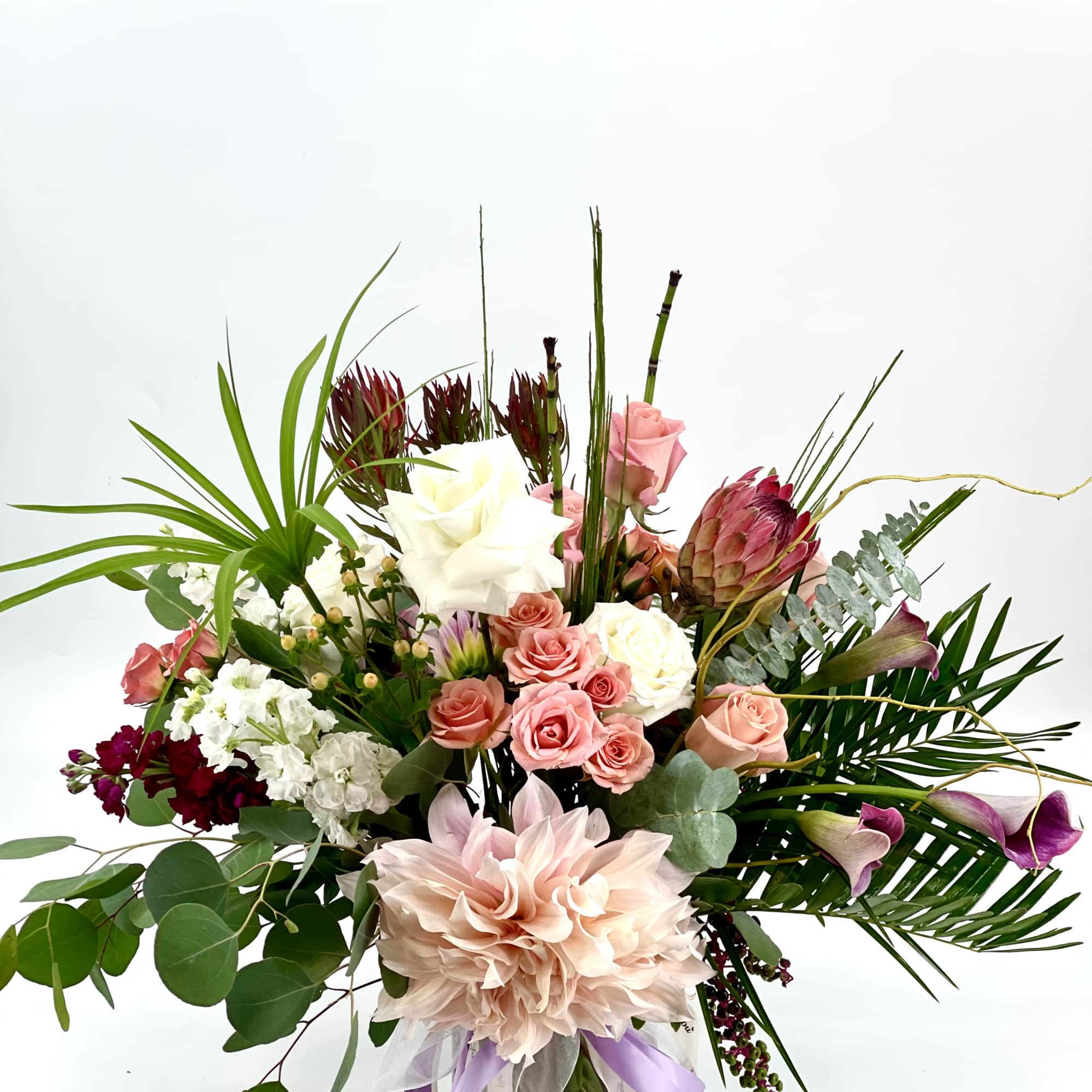 Mixed bouquet with roses, calla lilies, and a large pale dahlia in a glass vase
