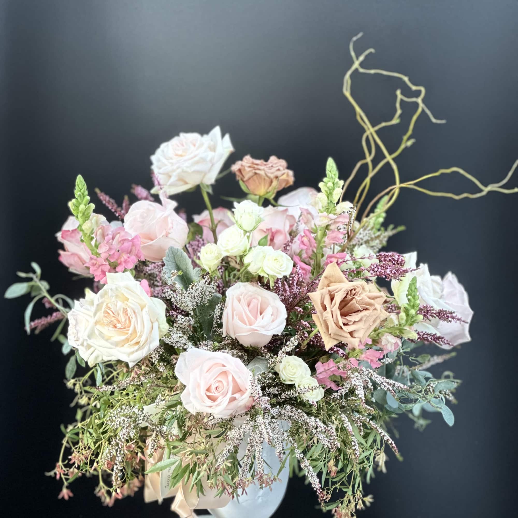Soft pastel arrangement of roses and snapdragons in a white pedestal urn with trailing fillers
