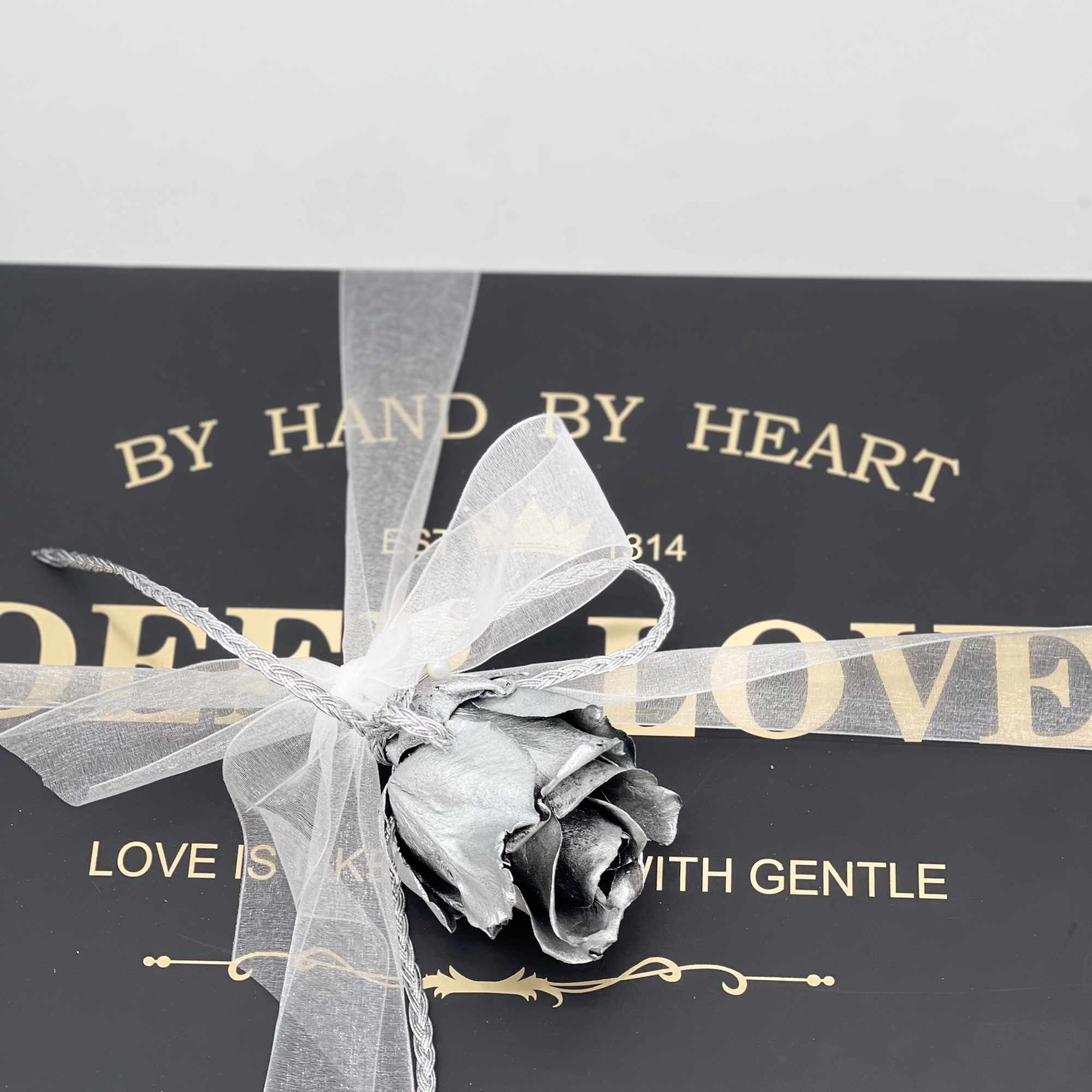 Single gray rose tied with a sheer ribbon on a black gift box